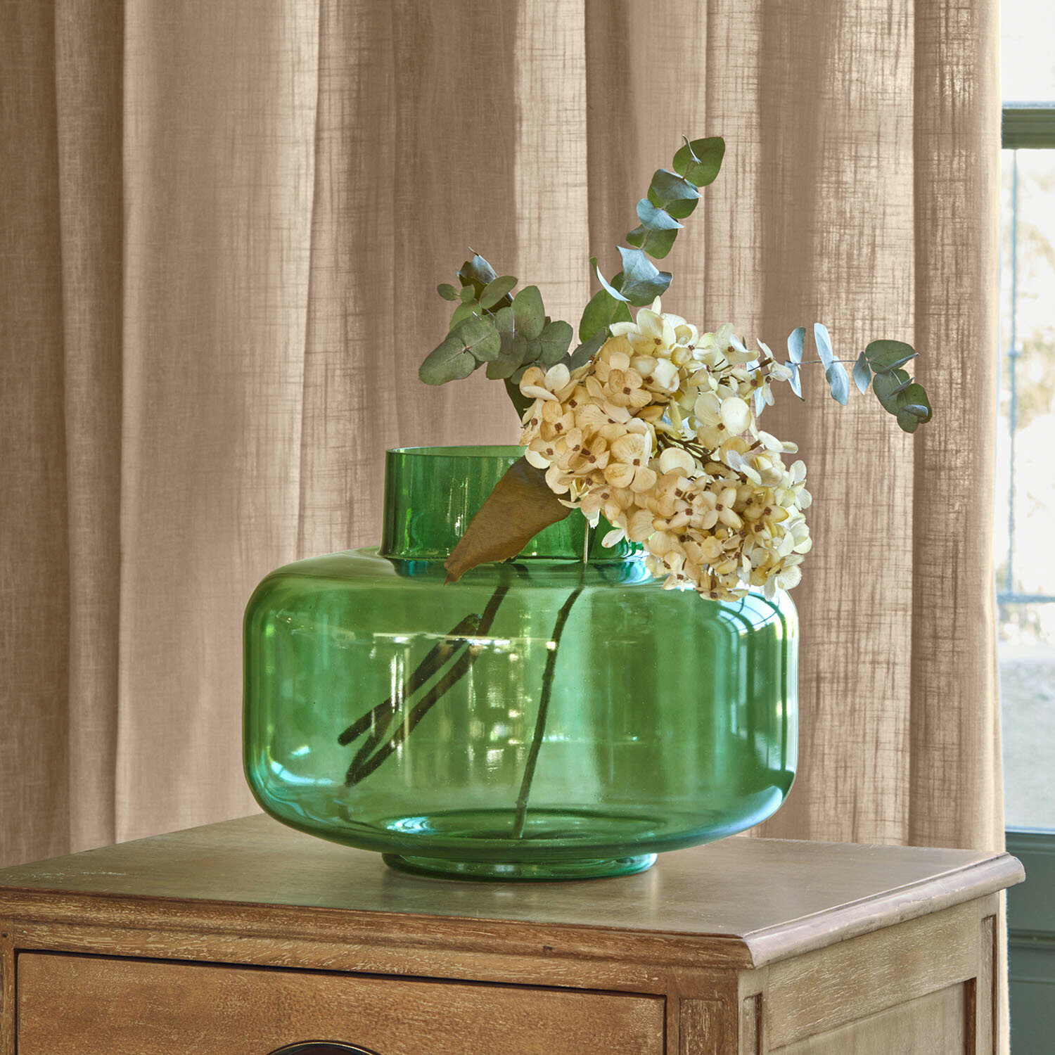 Jarrón Ésmarine Jarrón de vidrio verde con flores crema sobre mesa de madera, decoración de interiores