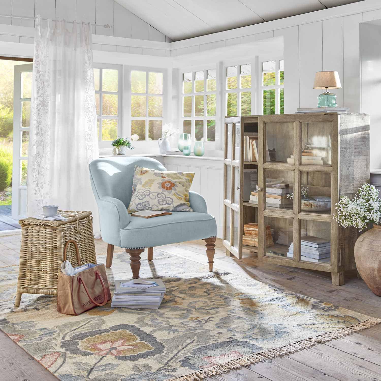 Sala acogedora con sillón azul claro, vitrina de madera y alfombra floral decorativa