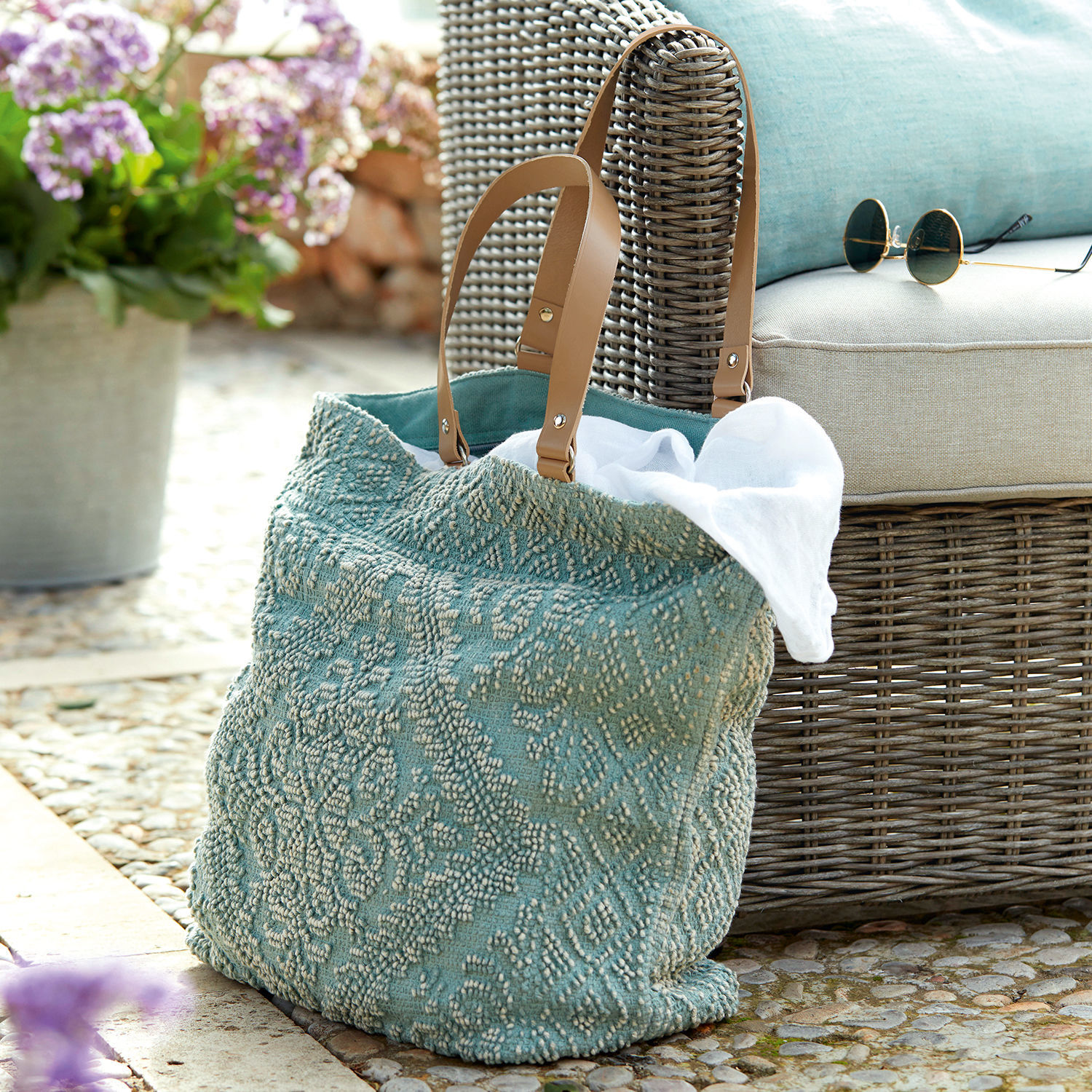 Bolso Vicel Bolso turquesa de tela texturizada con asas marrones junto a sillón de mimbre y gafas de sol