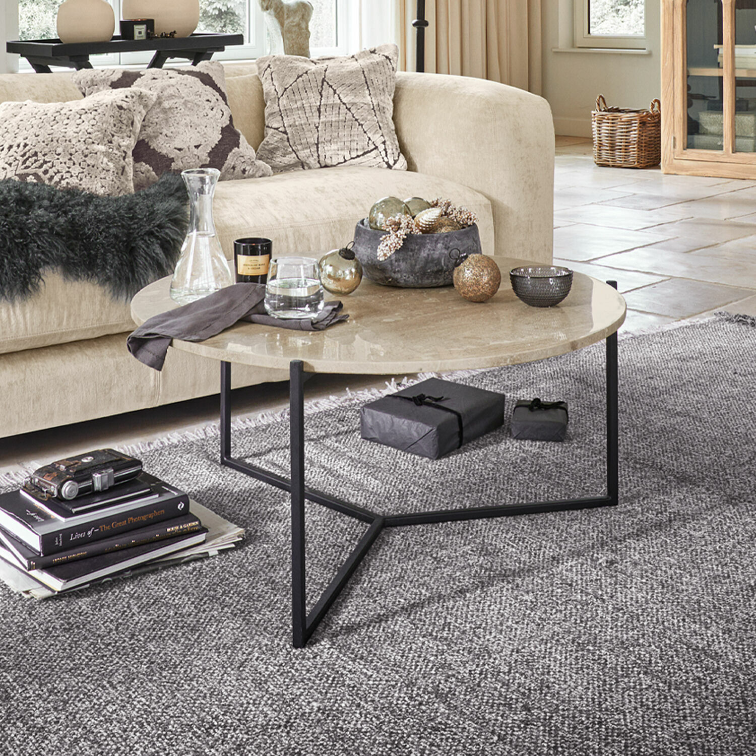 Mesa de centro Émorieux Mesa de centro redonda con tablero de mármol beige y base metálica negra sobre alfombra gris