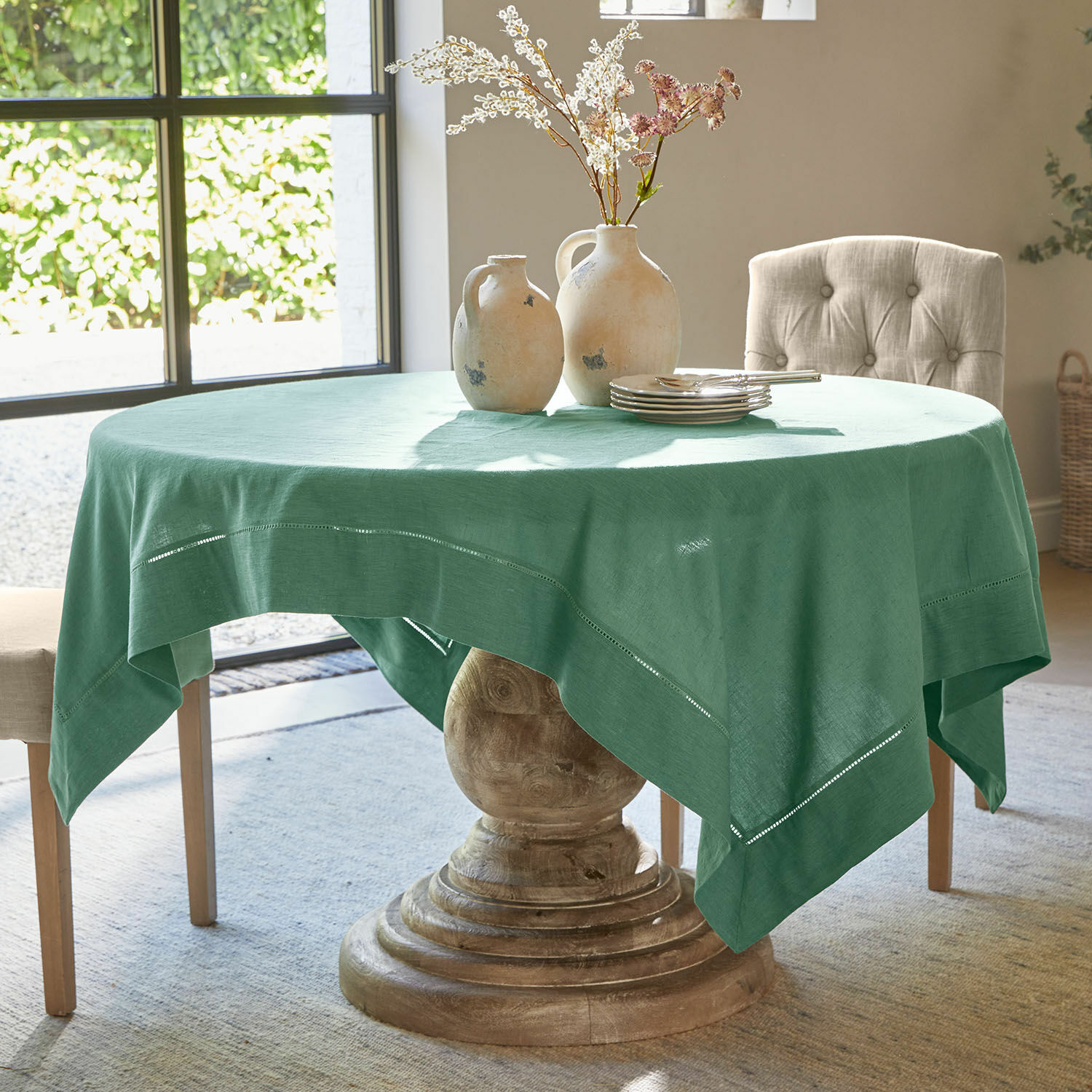 Mesa redonda con base de madera cubierta con mantel verde de lino con detalles decorativos