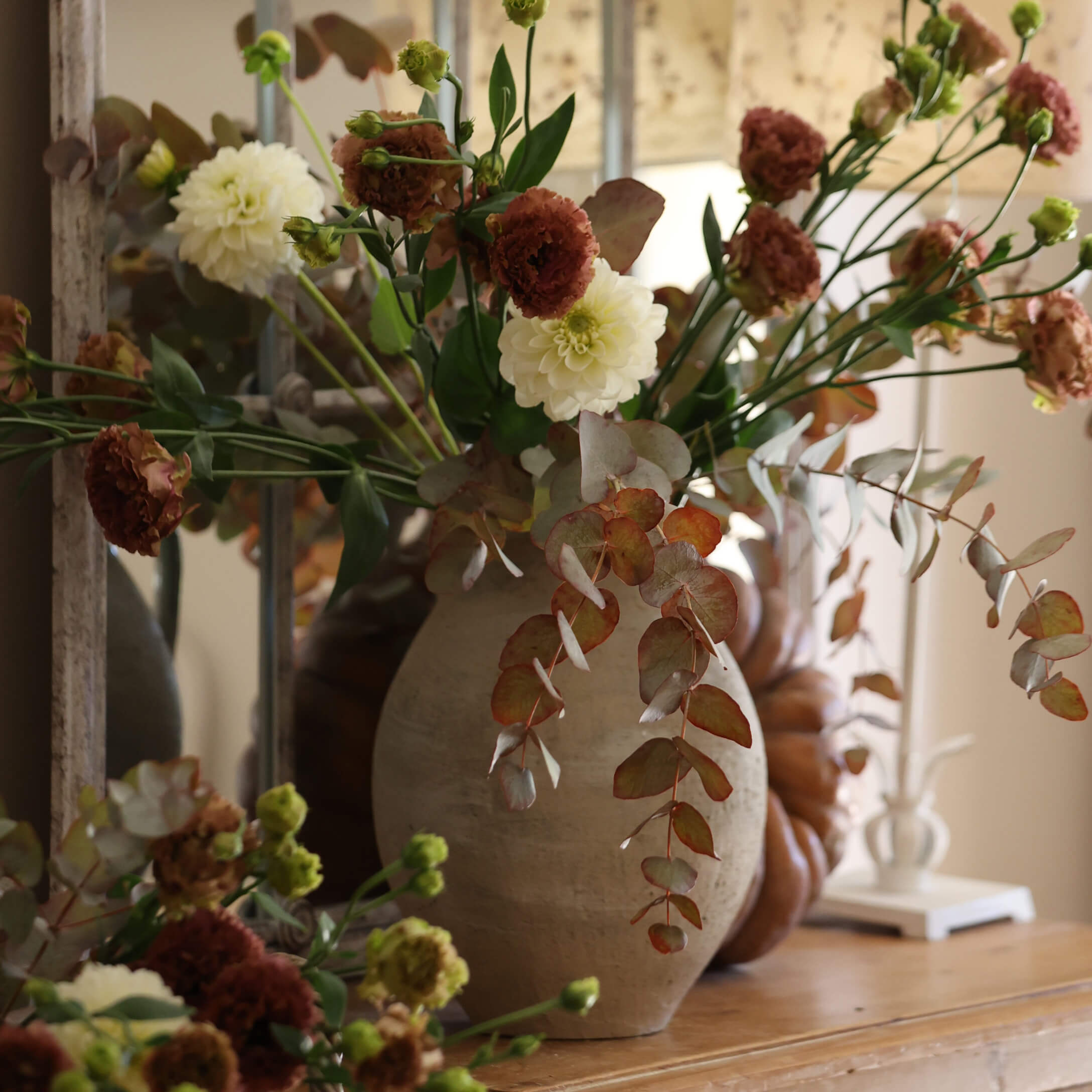 Jarrón de cerámica beige con ramo de flores blancas y marrones sobre mesa de madera decorativa
