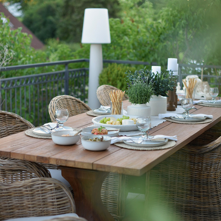 Mesa de jardín de madera con sillas de mimbre y decoración para comida de verano en terraza