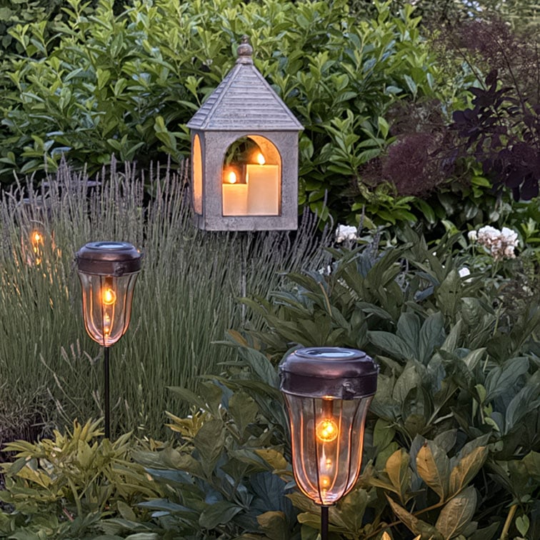 Jardín con luces solares y farol colgante con velas decorativas, iluminación exterior