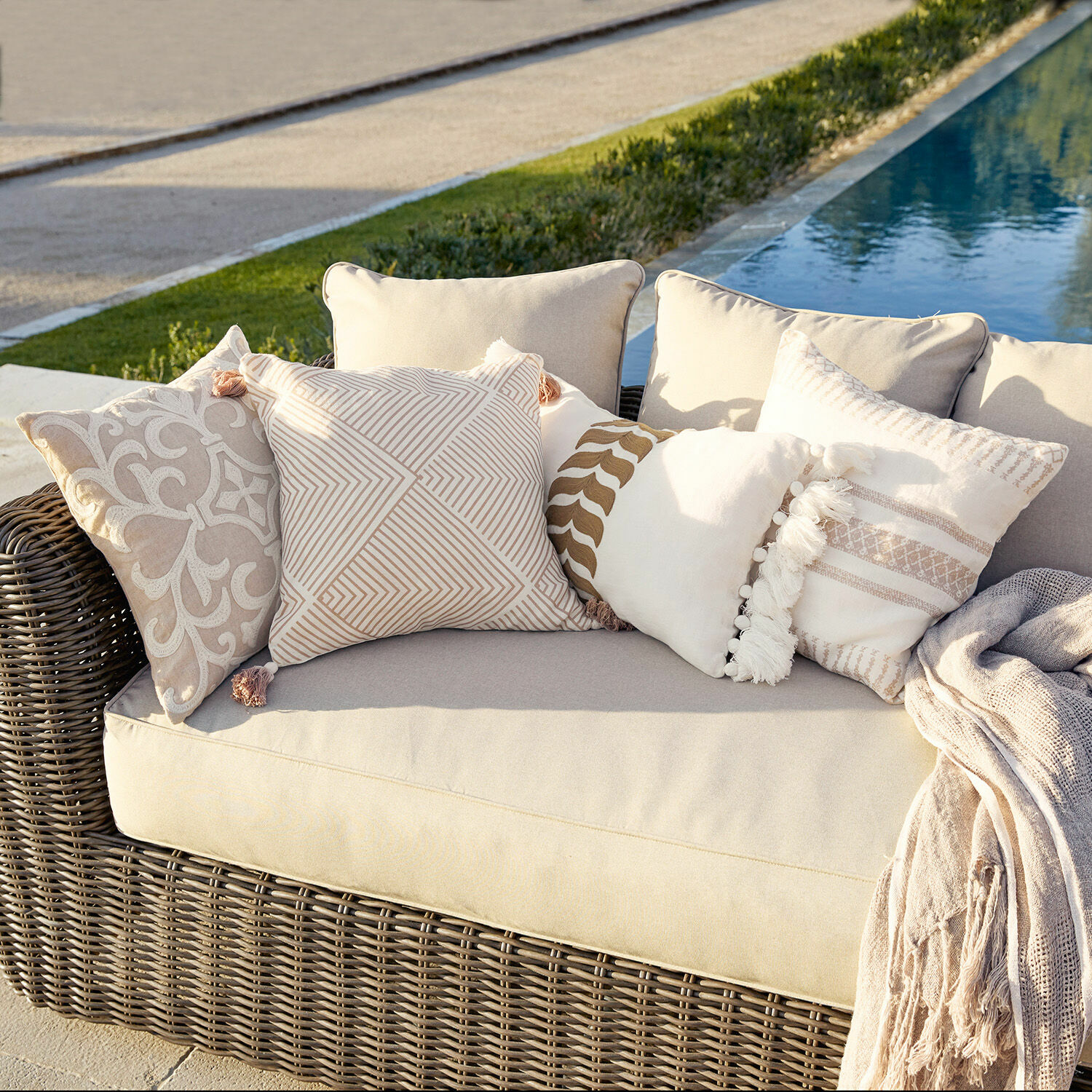 Set de 4 fundas de cojín Olette Sofá de ratán beige con cojines decorativos crema y beige al aire libre junto a la piscina