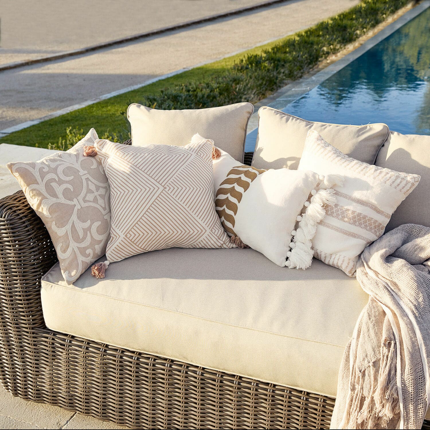 Set de 4 fundas de cojín Olette Sofá de ratán beige con cojines decorativos crema y beige al aire libre junto a la piscina