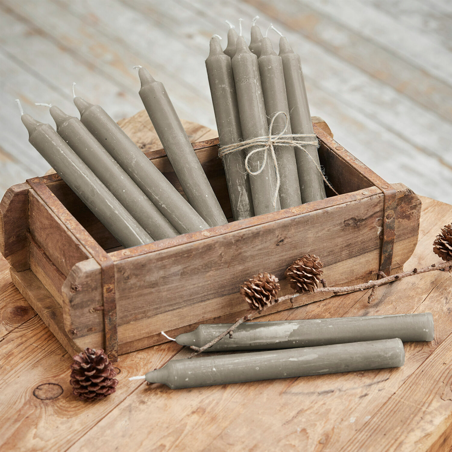 Set de 12 velas Bauceau Velas de mesa grises de cera en caja de madera sobre mesa rústica con piñas