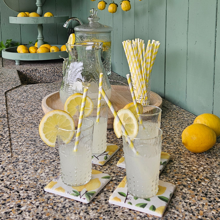 Vasos con limonada y rodajas de limón sobre encimera de piedra con pajitas de papel y bandeja con limones