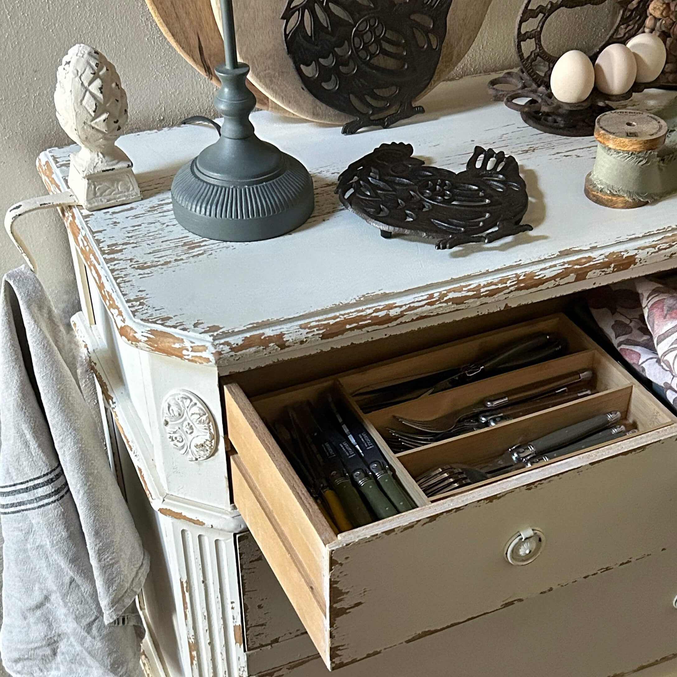 Cómoda de madera blanca envejecida con cajón abierto y cubiertos organizados, estilo rústico