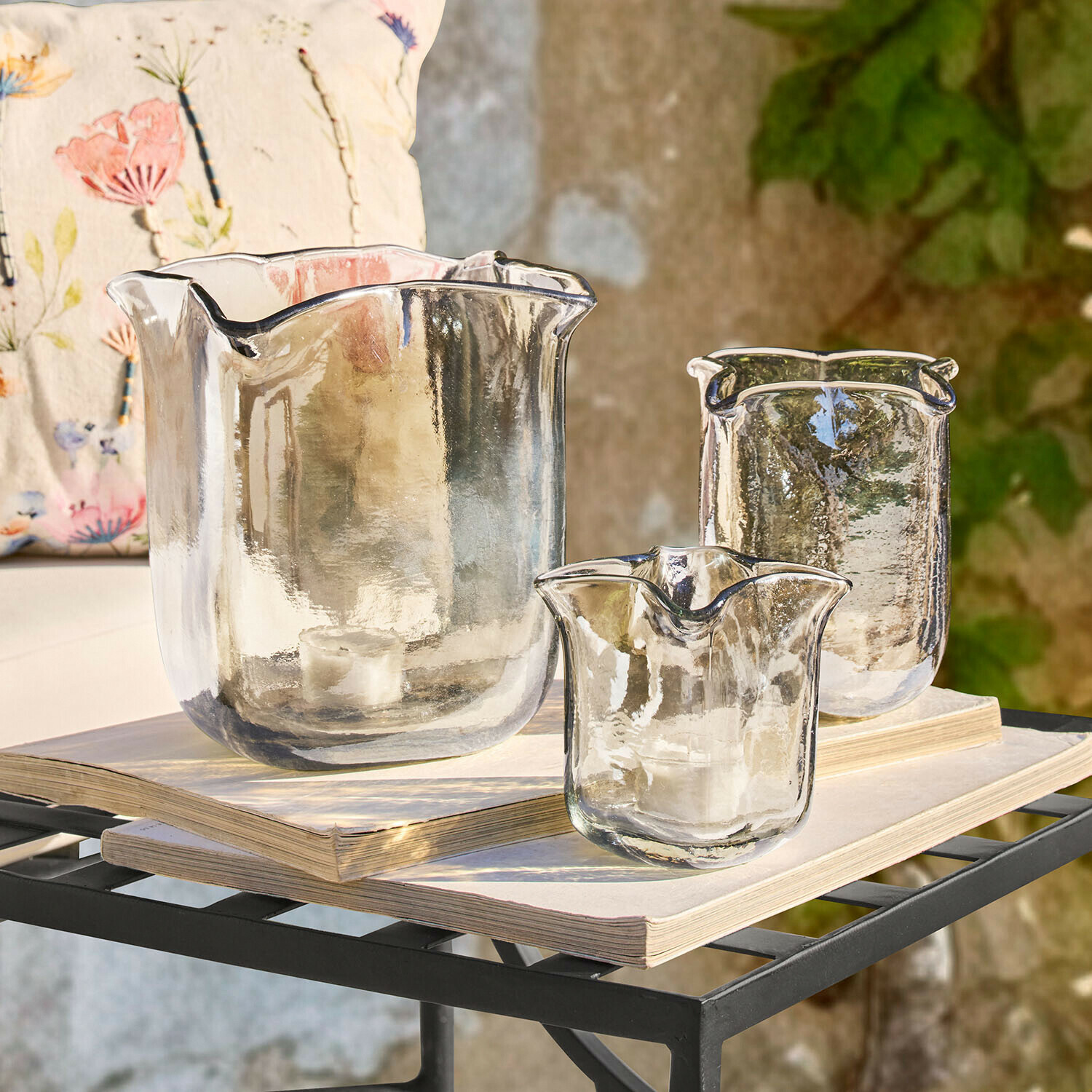 Conjunto de tres portavelas de vidrio transparente con forma irregular sobre libros