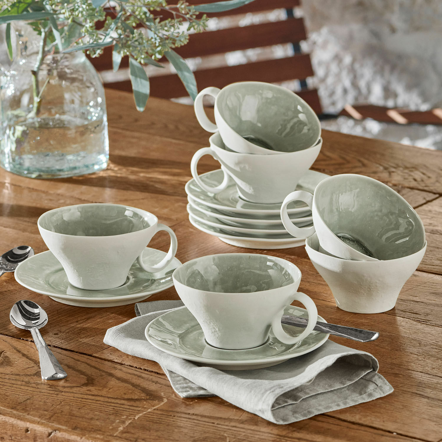 Set de 6 tazas con platillos Braganza Juego de tazas de cerámica blanca con interior verde sobre mesa de madera con cucharas