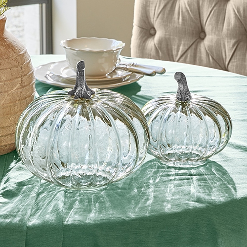 Decoraciones de cristal en forma de calabazas con tallos metálicos sobre mantel verde, adorno de mesa