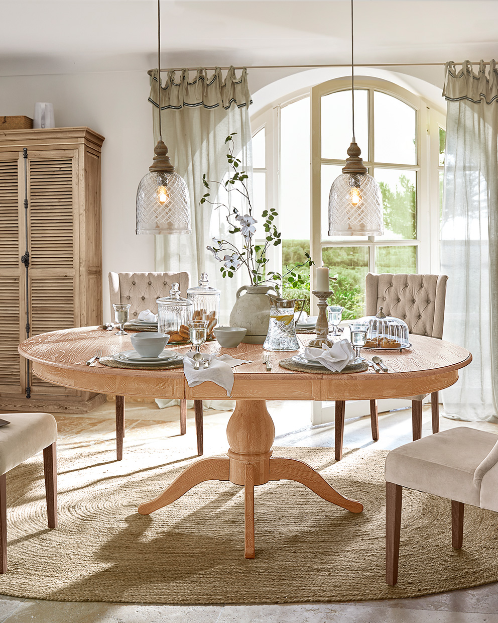 Mesa de comedor ovalada de madera clara con sillas beige y decoración de mesa en estilo rústico