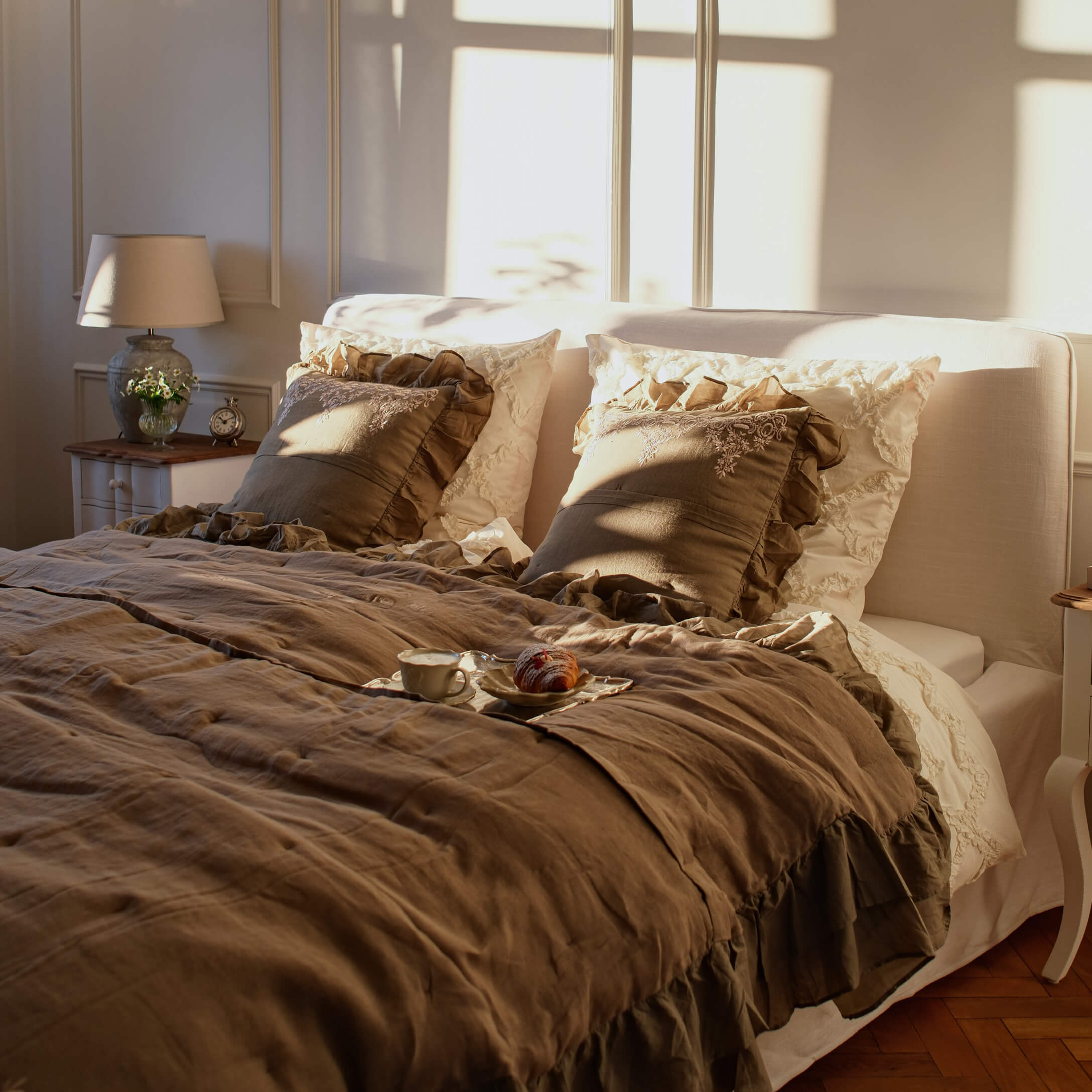 Dormitorio acogedor con ropa de cama de lino beige y cojines marrones con volantes bajo luz cálida