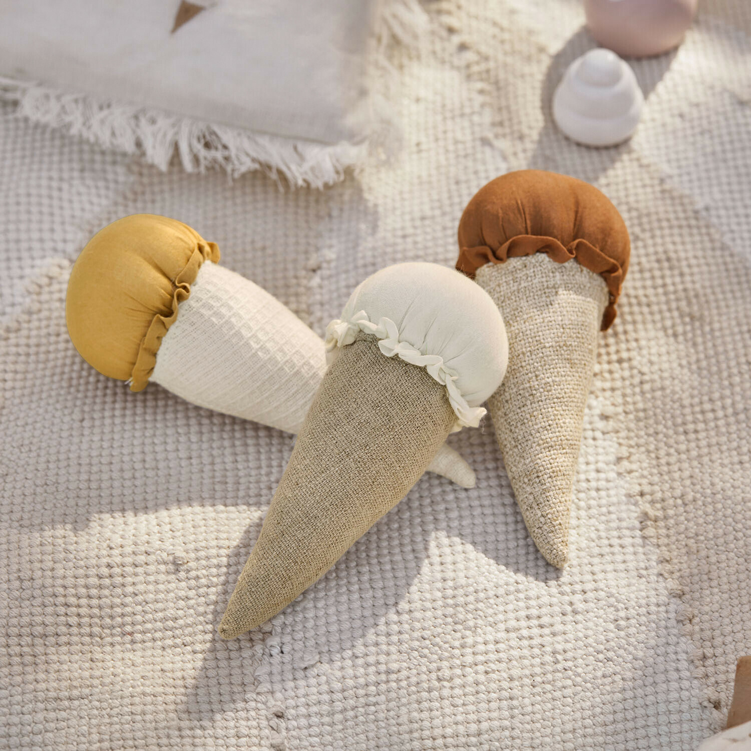 Tres juguetes de tela en forma de conos de helado en tonos beige, blanco y marrón sobre una alfombra clara