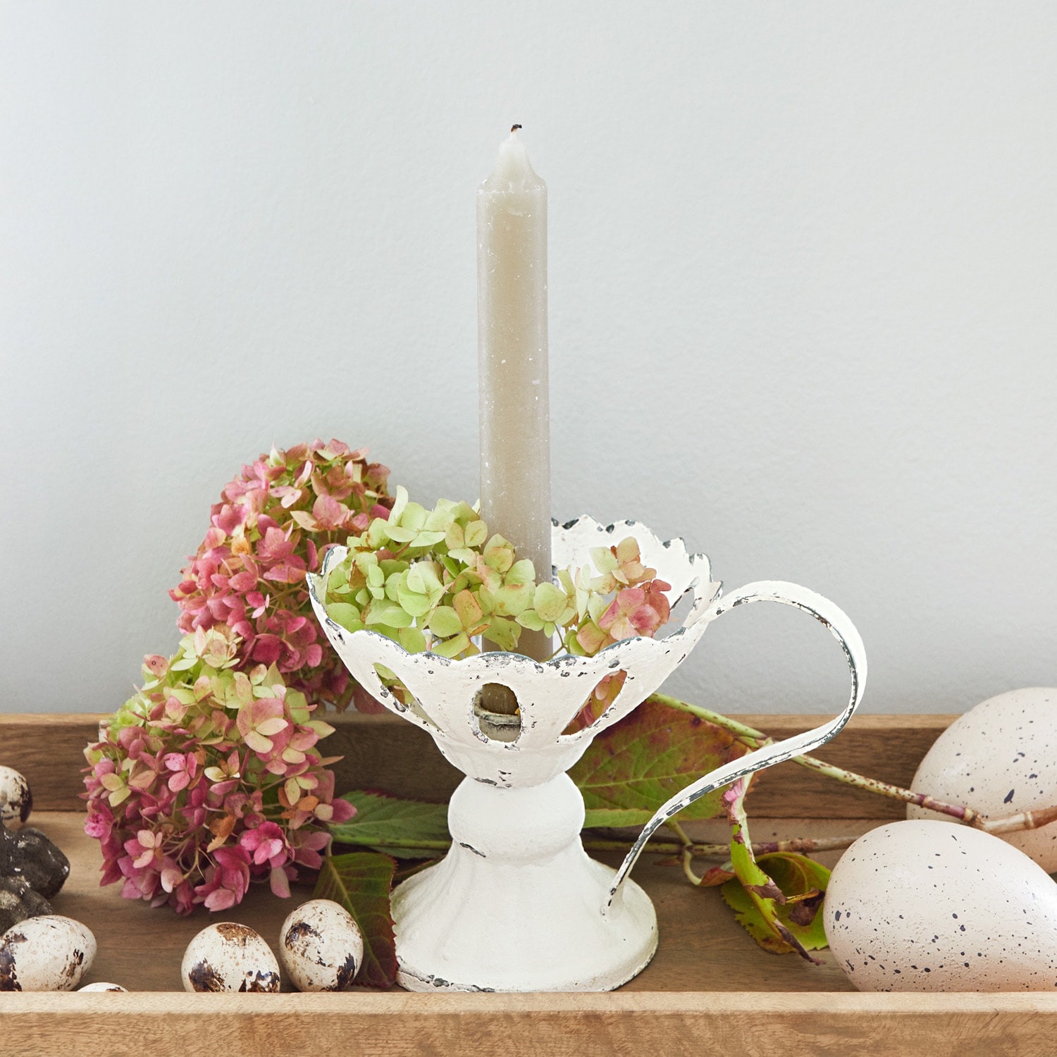 Candelabro metálico blanco con asa y vela gris, decorado con flores y huevos decorativos