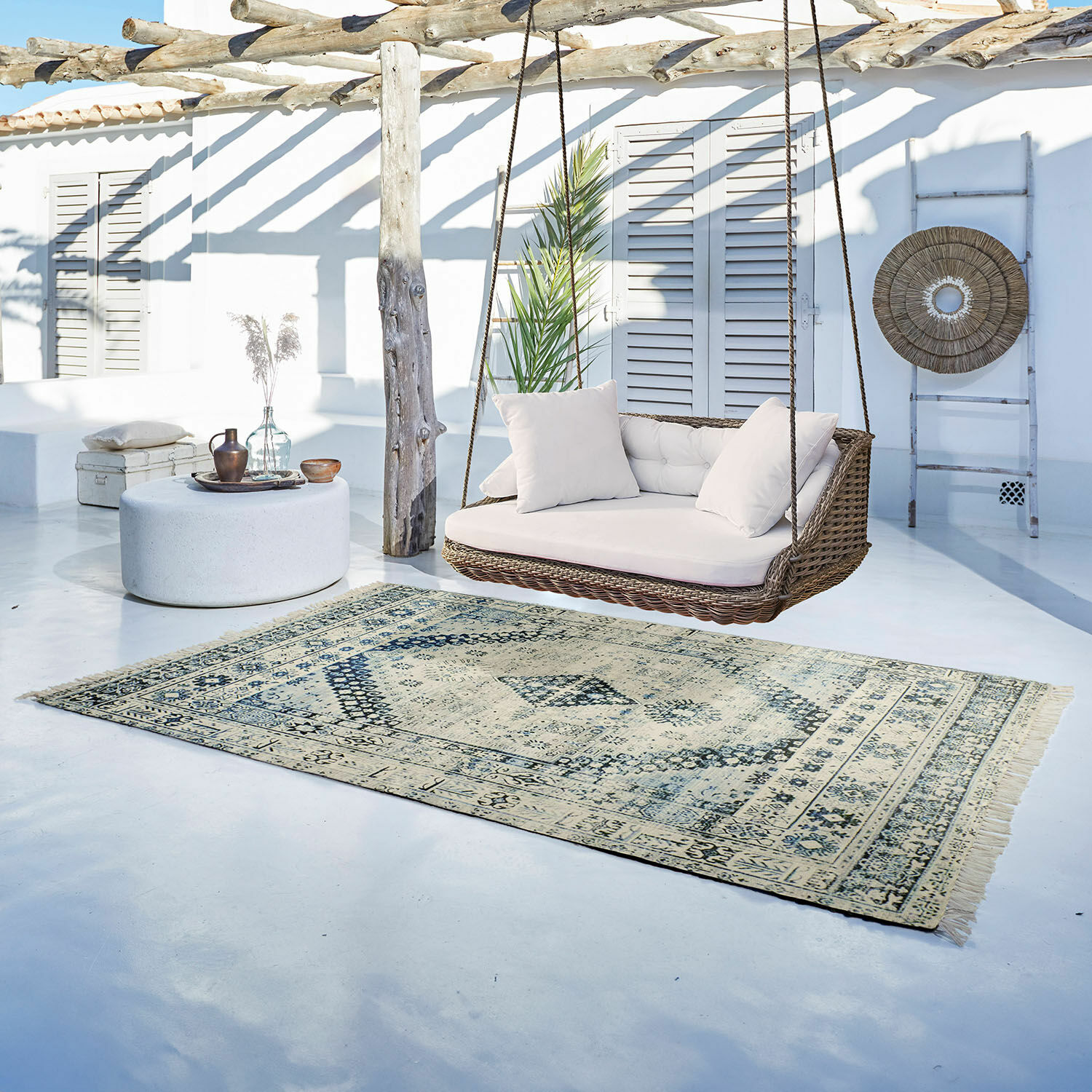 Alfombra para interior y exterior Daly Alfombra vintage beige y azul claro sobre suelo claro junto a columpio de ratán con cojines blancos