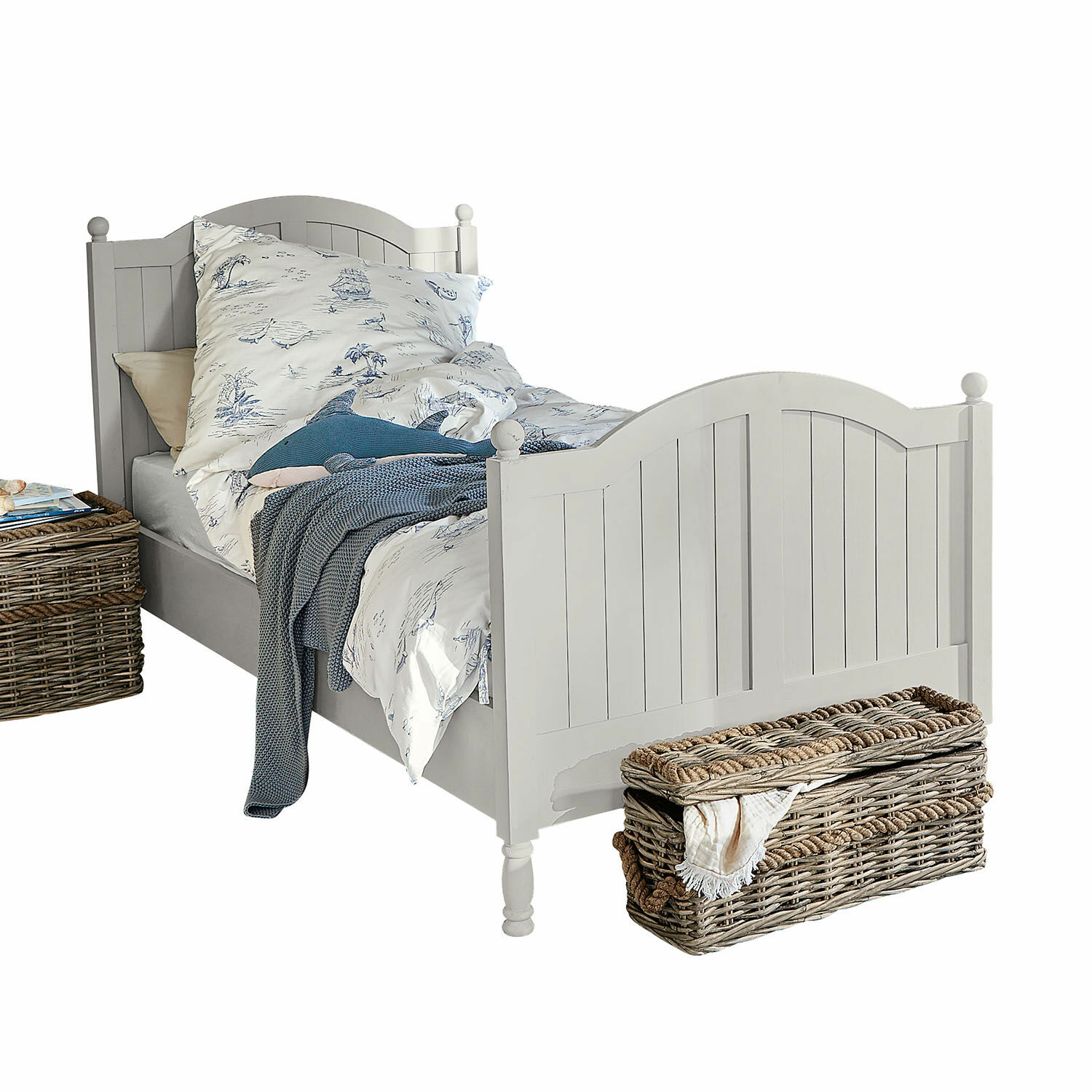 Cama Alarion Cama de madera blanca con cabecero decorativo, ropa de cama con motivos azules y cesta de mimbre al lado