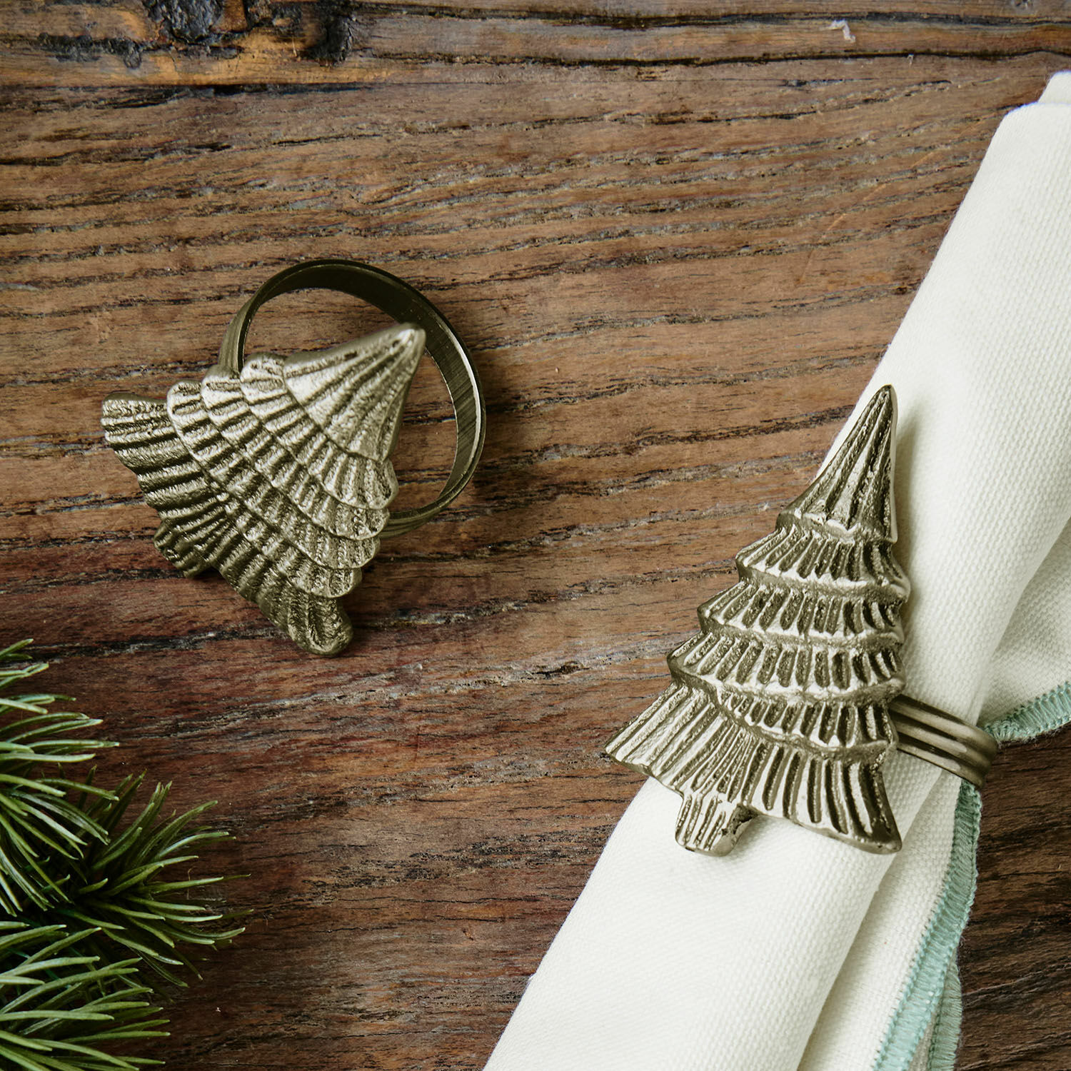 Set de 2 servilleteros Sylvion Anillos de servilleta metálicos con forma de árbol de Navidad en color plata envejecida sobre mesa de madera