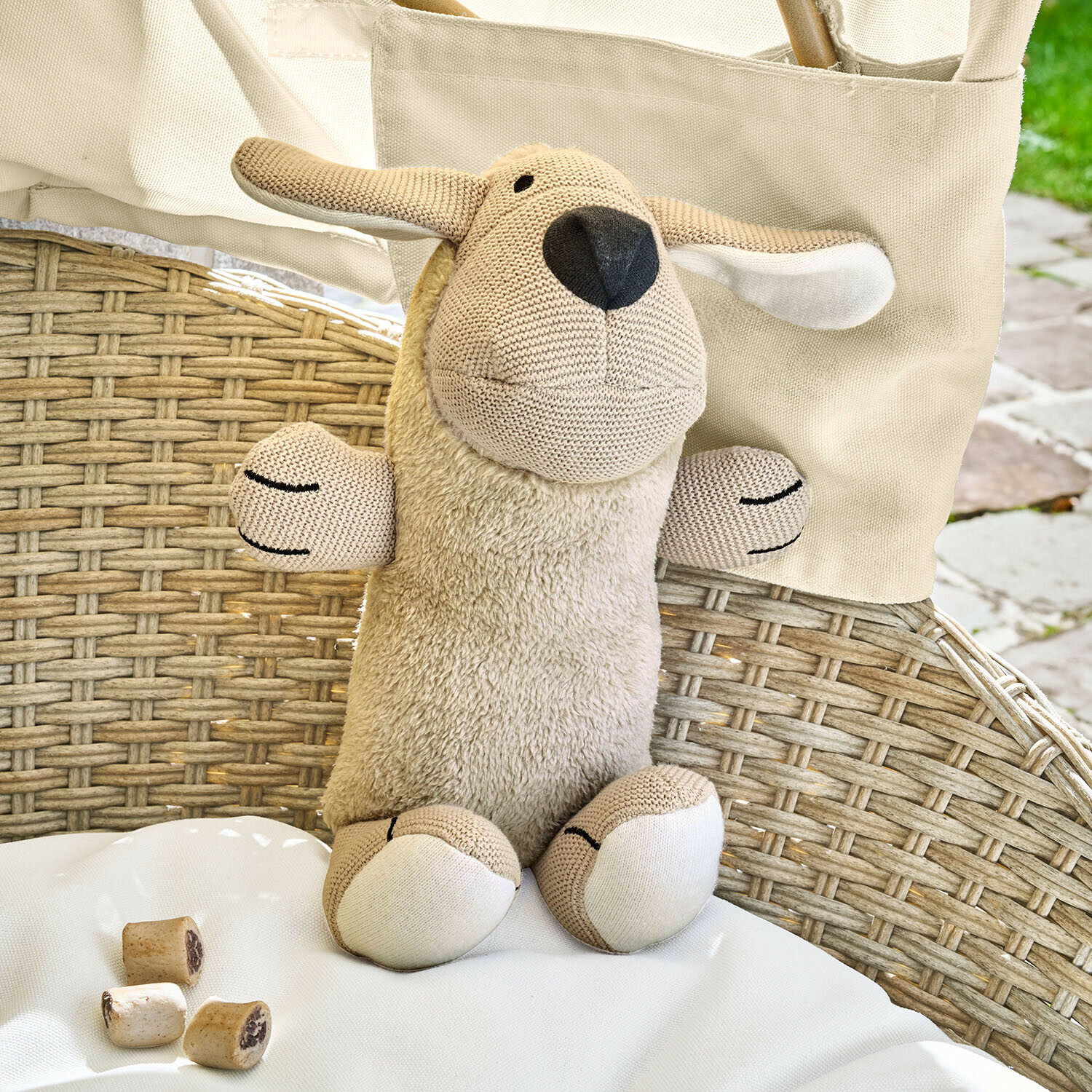 Peluche de oveja beige con cuerpo de felpa suave y detalles de punto sobre silla de ratán
