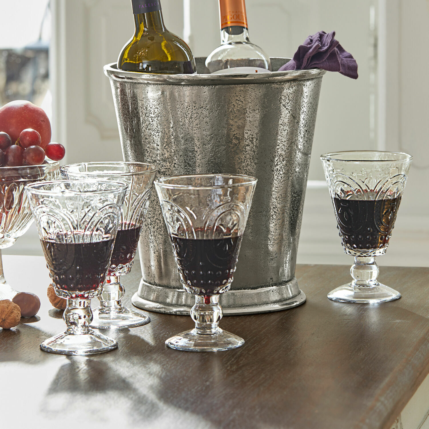 Cubitera metálica con dos botellas de vino y cuatro copas de cristal con vino tinto sobre mesa de madera