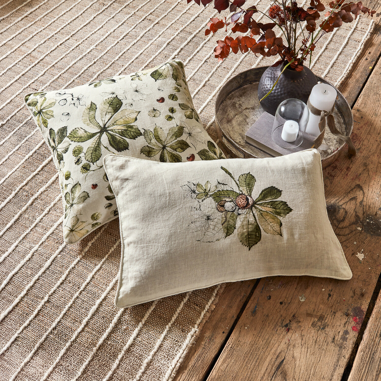 Set de 2 fundas de cojín Elsie Cojines decorativos de lino con hojas verdes sobre fondo beige en alfombra y suelo de madera