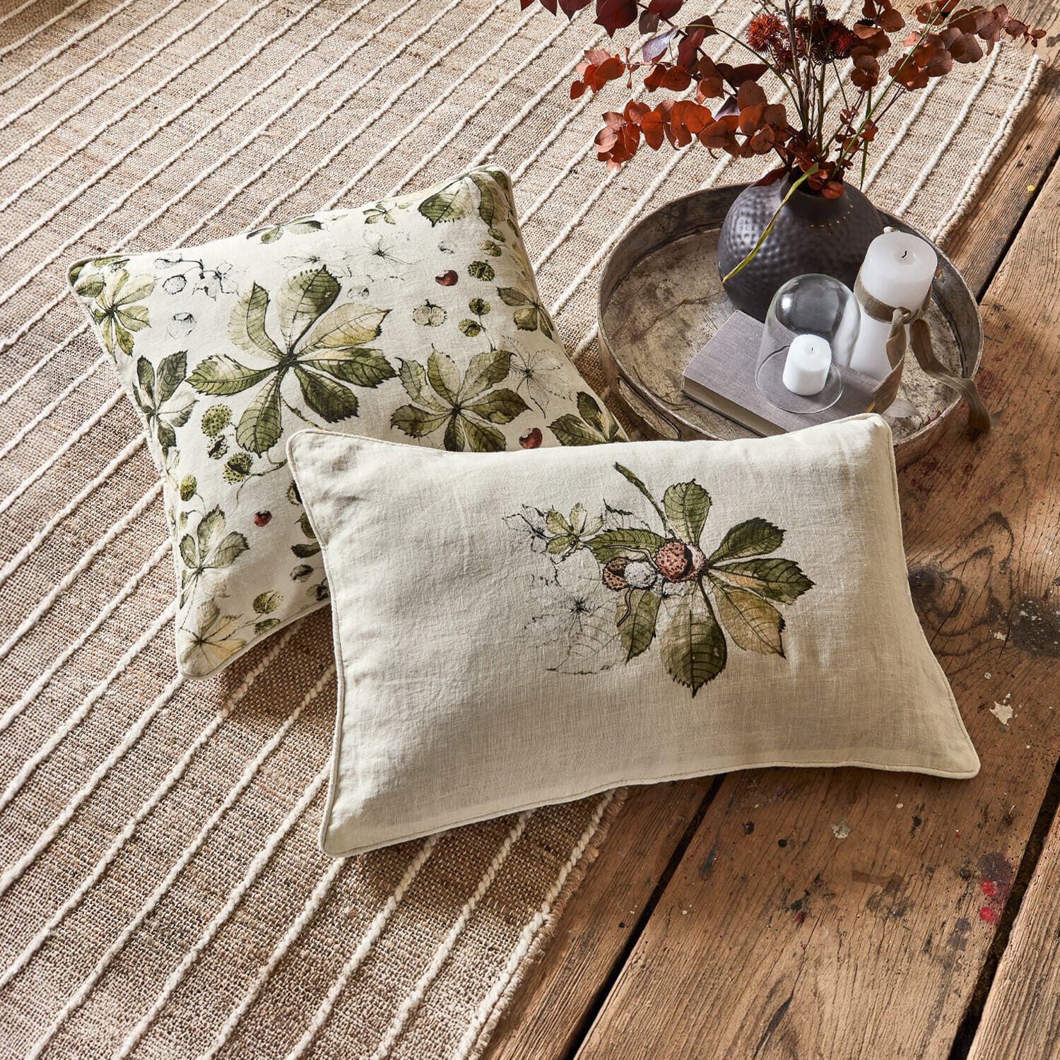 Set de 2 fundas de cojín Elsie Cojines decorativos de lino con hojas verdes sobre fondo beige en alfombra y suelo de madera
