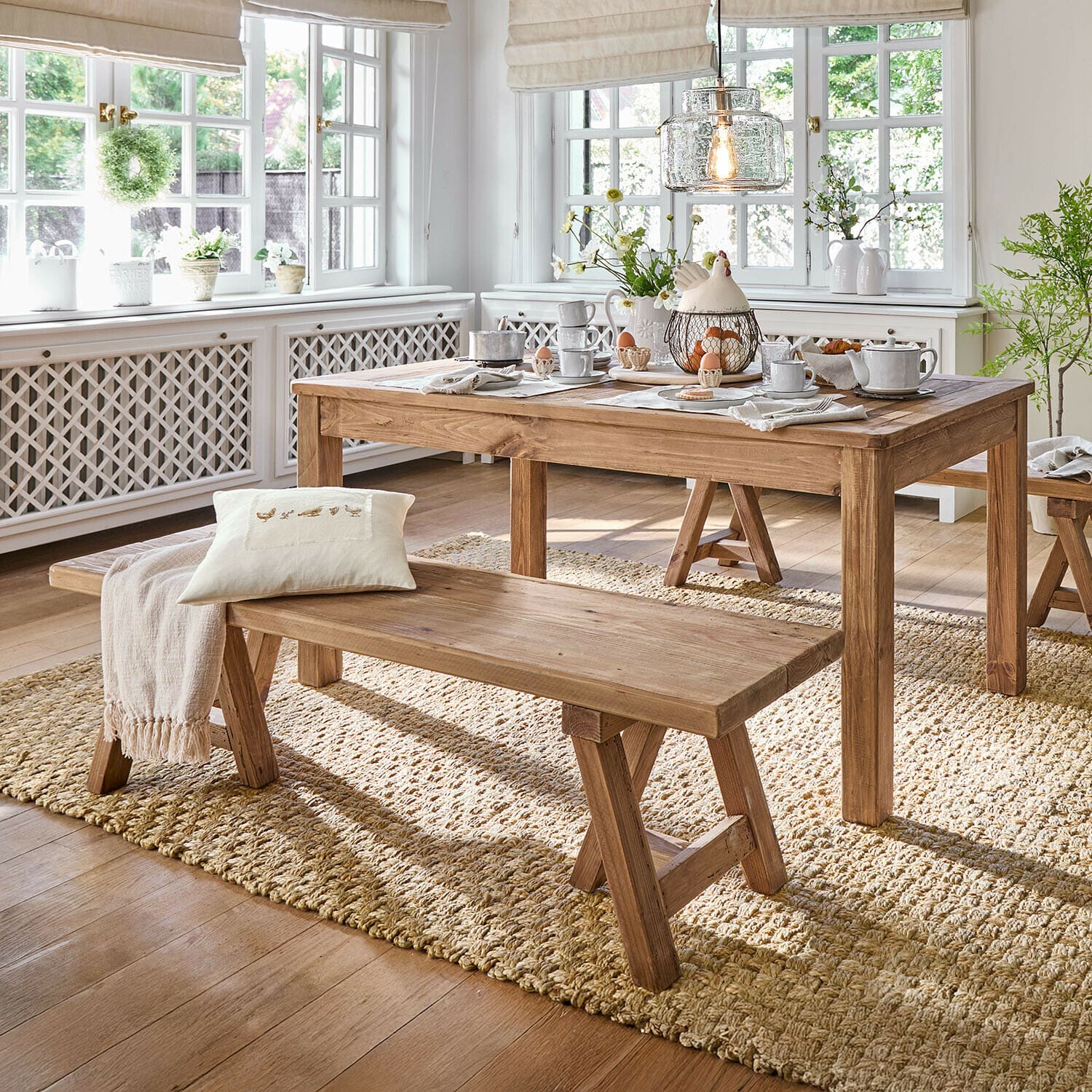 Banco Amherst Comedor con mesa y banco de madera sobre alfombra natural, interior luminoso con grandes ventanas