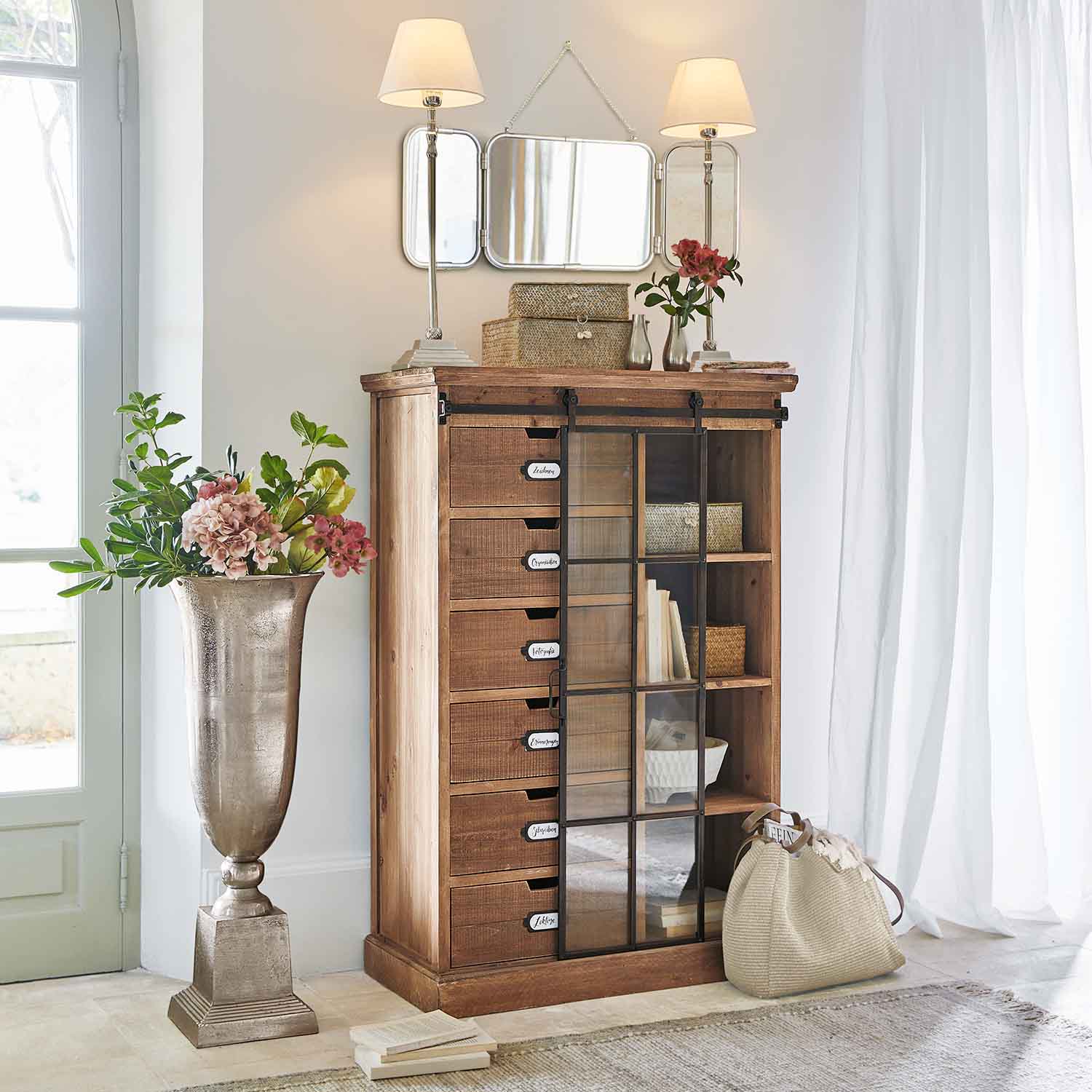 Cómoda de madera con cajones y puerta de cristal en interior luminoso con decoración y lámparas