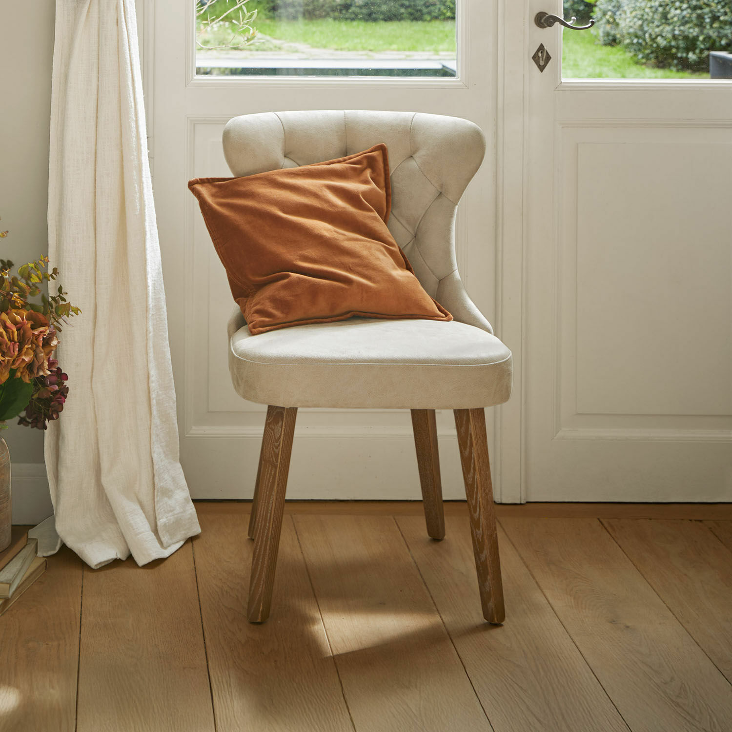 Silla tapizada beige con patas de madera y cojín naranja en interior luminoso