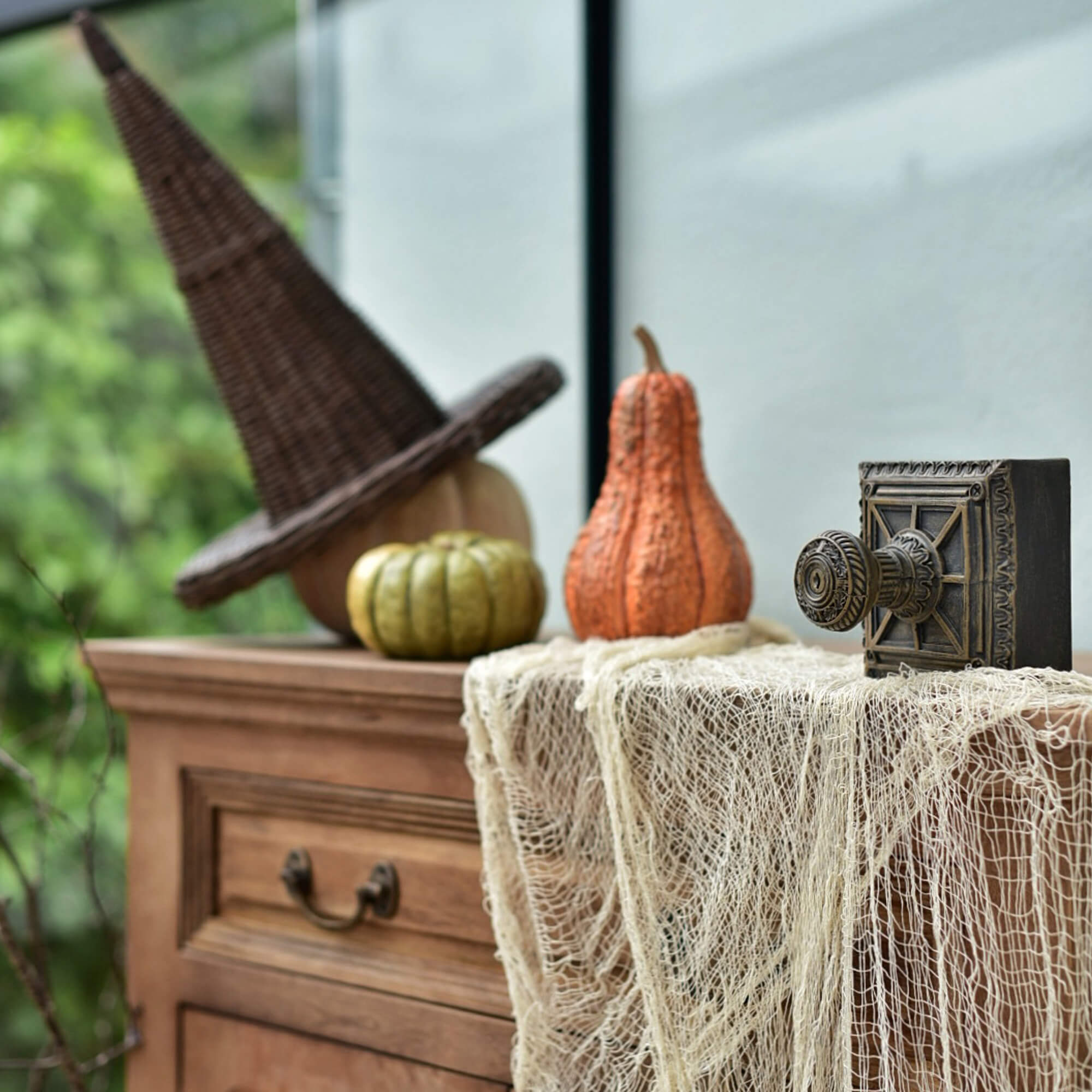Cómoda de madera con sombrero de bruja de mimbre y calabazas para decoración de Halloween