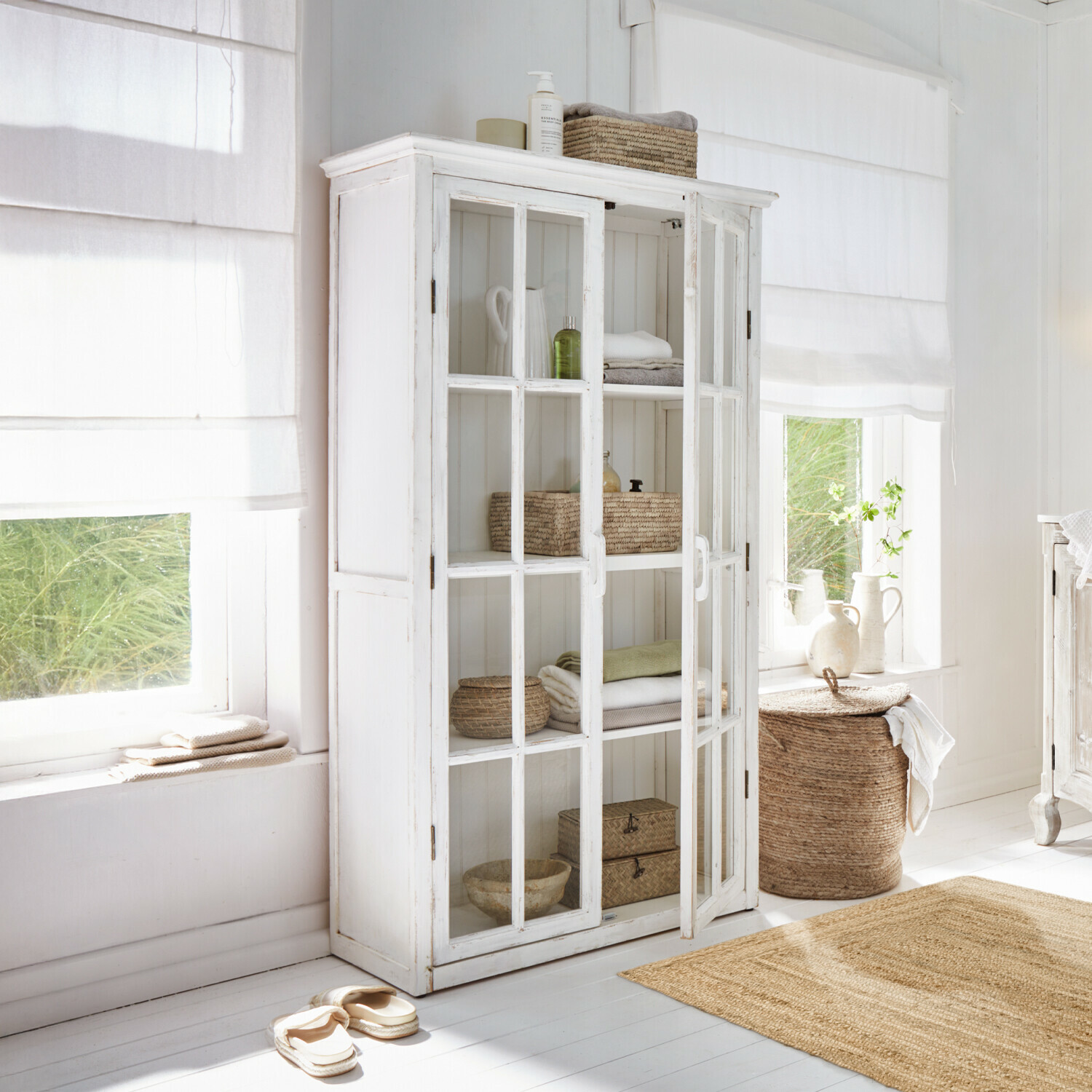 Armario Keanu Vitrina blanca de madera con puertas de cristal en habitación luminosa con decoración natural y textiles
