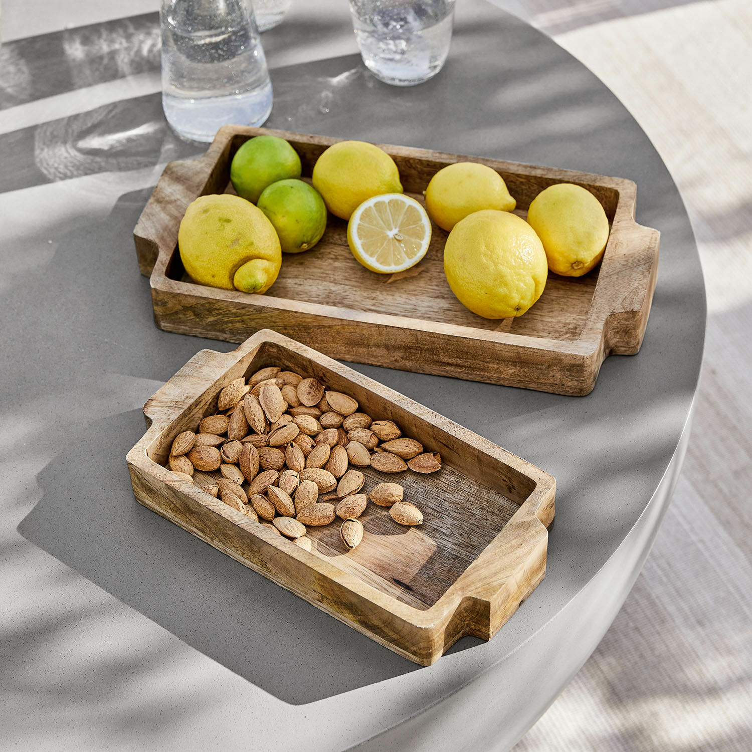 Set de 2 bandejas Buer Bandejas rectangulares de madera con asas, una con limones y otra con almendras sobre mesa gris