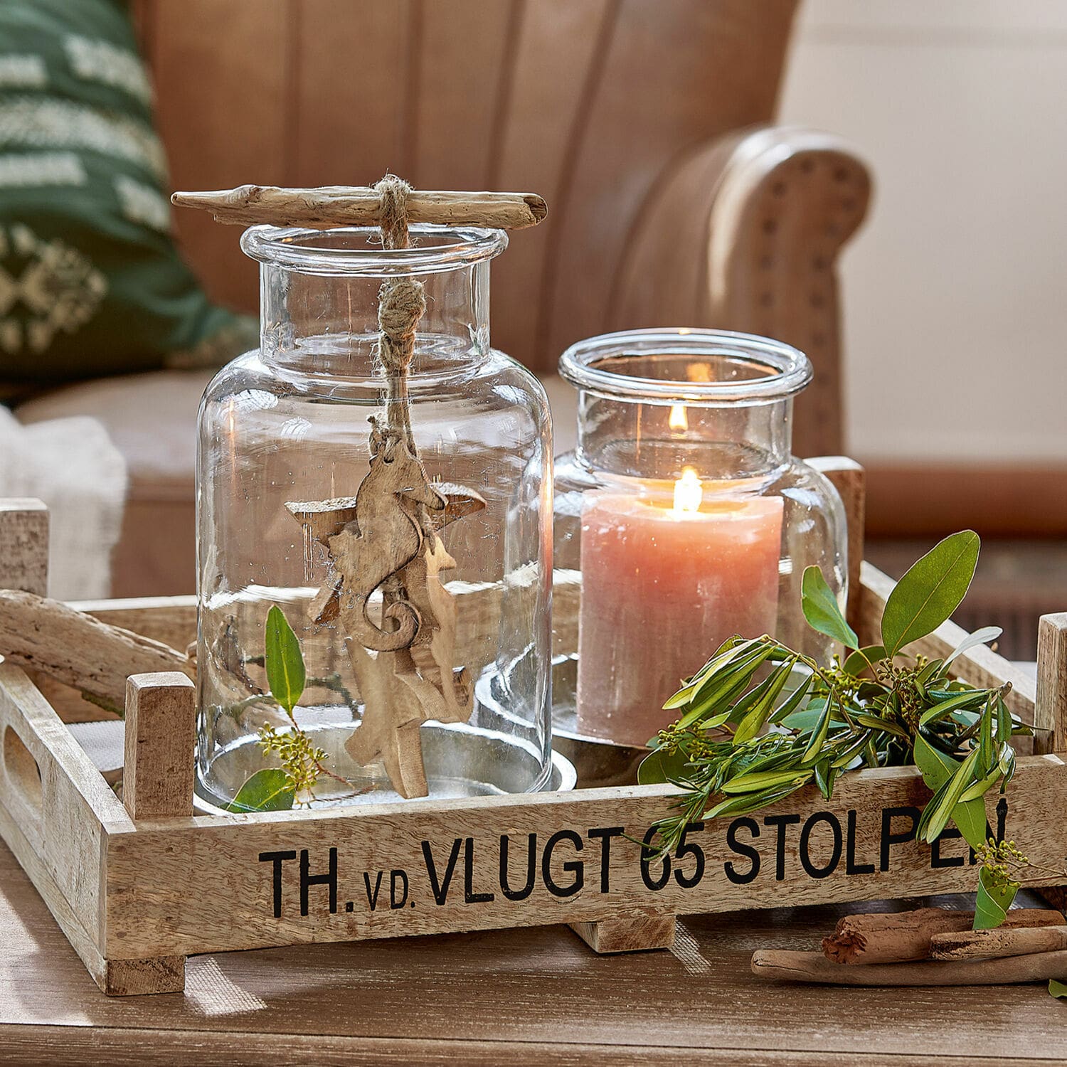 Set de 2 farolillos Emphoria Bandeja de madera con portavelas de vidrio transparente y decoración de hojas verdes sobre mesa de madera