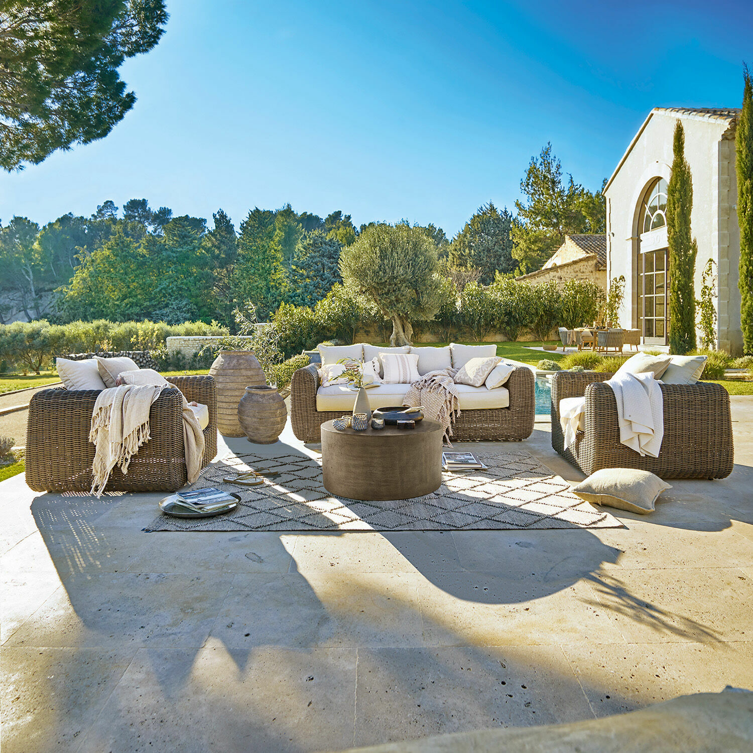 Grupo de asientos Bogdanne Conjunto de muebles de jardín de ratán marrón con cojines crema en terraza con vista al jardín