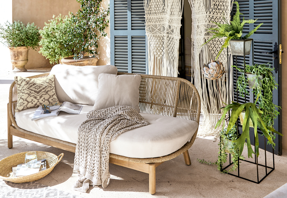 Sofá bohemio con tapizado beige claro y estructura de madera, decorado con cojines y manta tejida