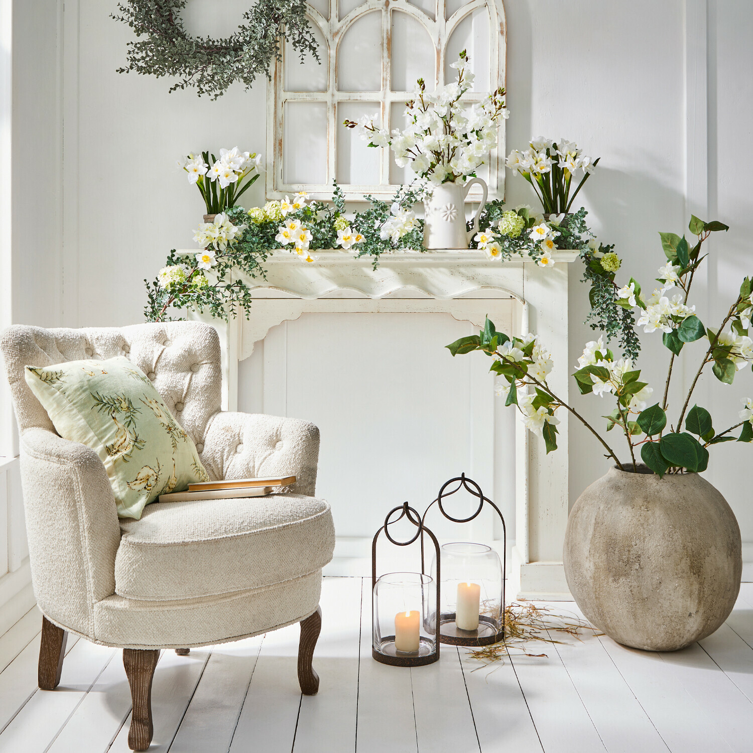 Consola de chimenea Claybourne Sillón crema cómodo con patas de madera junto a chimenea decorativa con flores blancas y velas