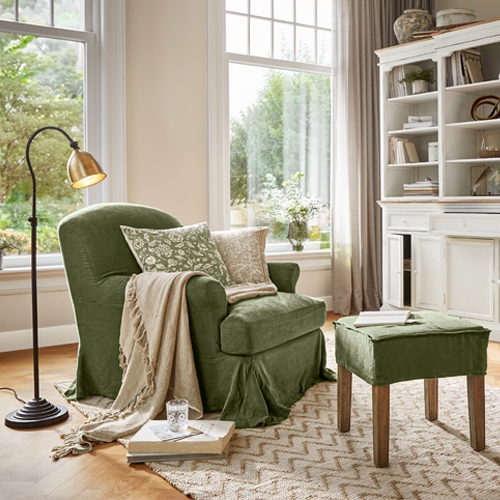 Sillón verde de tela con reposapiés y manta beige en sala luminosa con ventana grande