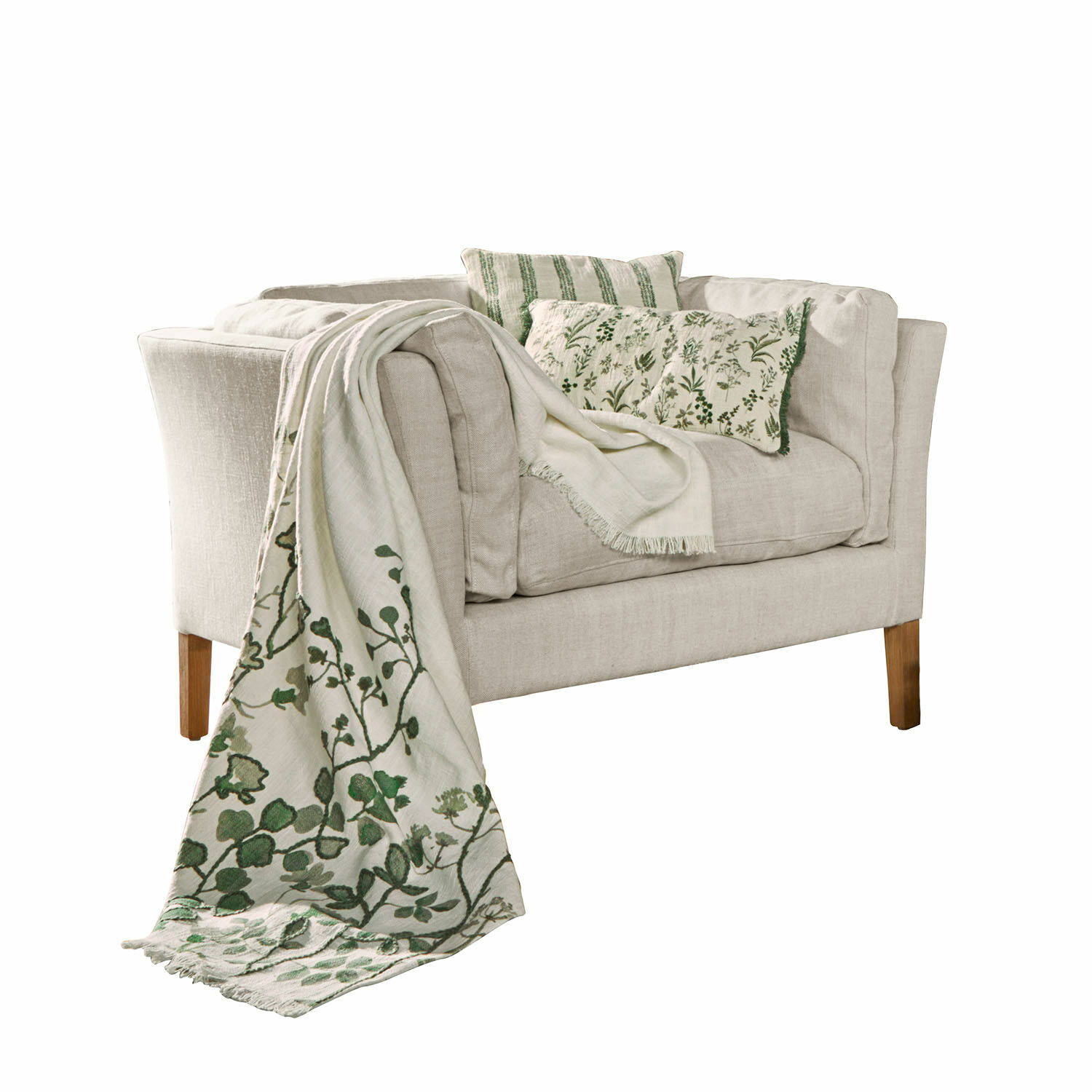Sofá beige de tela con cojines verdes y manta decorativa con diseño vegetal