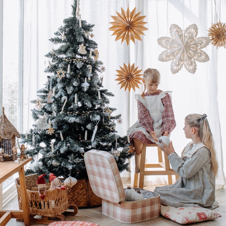 Niños junto a un árbol de Navidad decorado con adornos naturales y estrellas de papel en una habitación luminosa