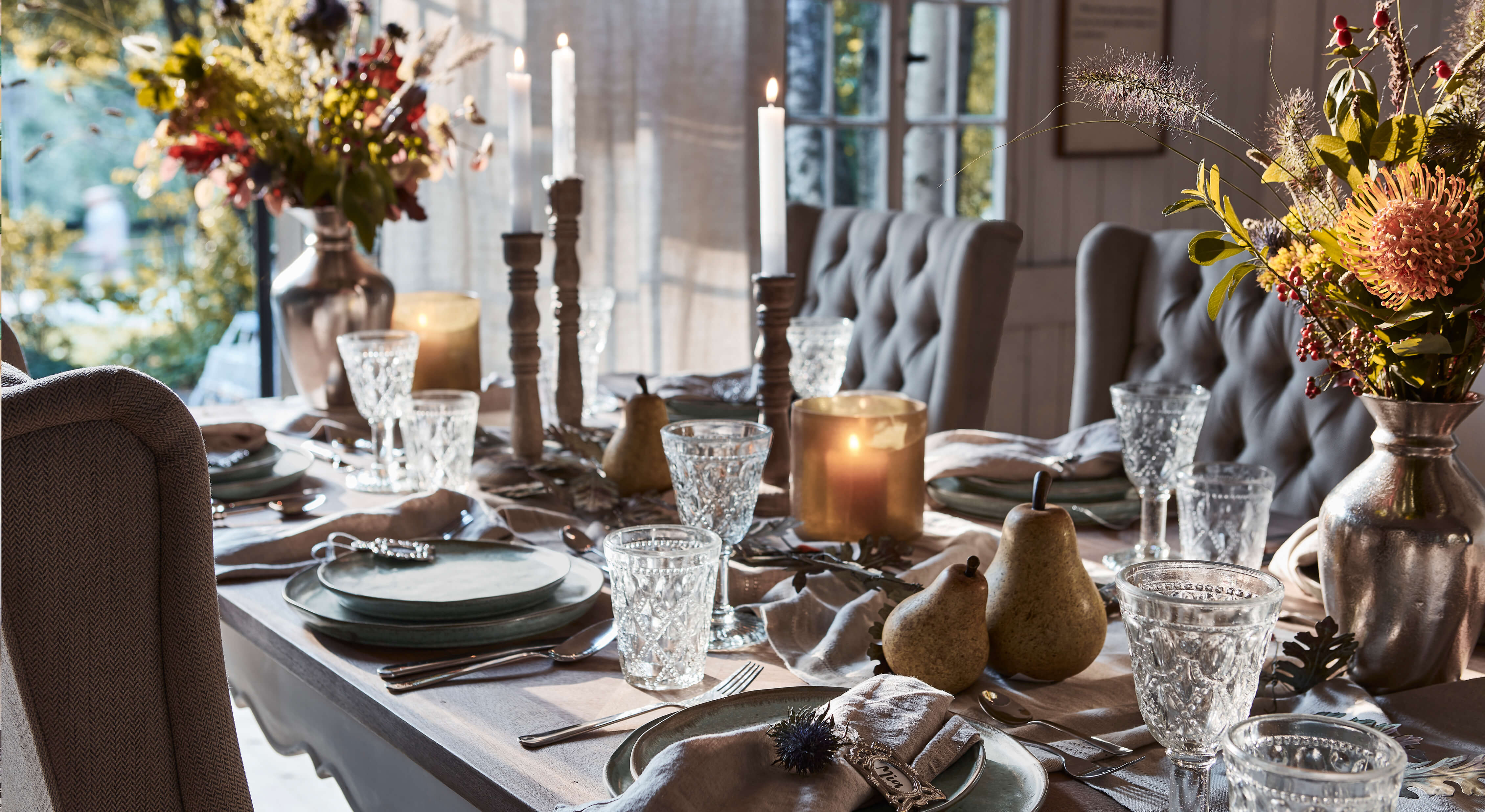 Mesa elegantemente puesta con platos grises, copas de cristal y velas en un ambiente acogedor