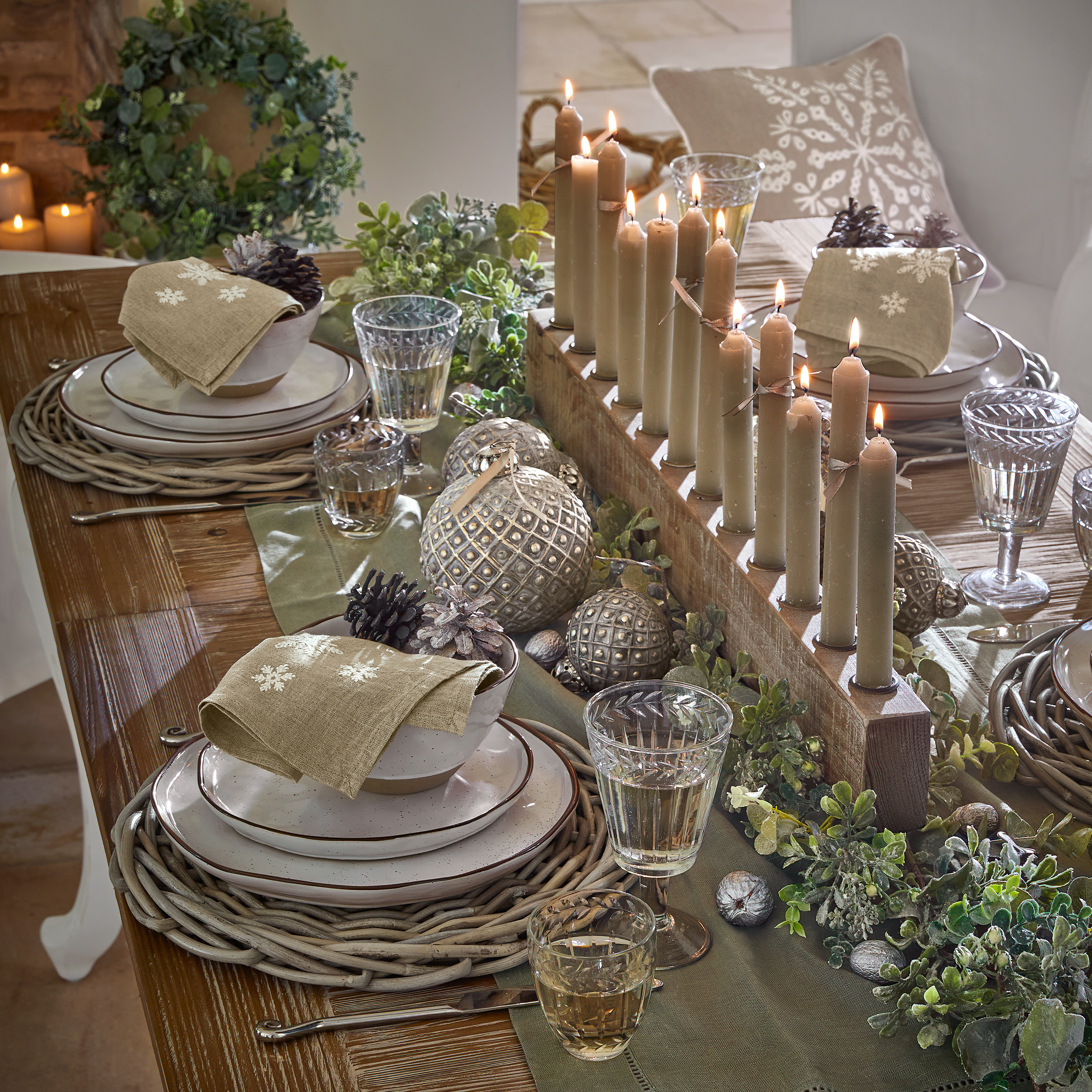 Mesa rústica de madera con decoración de velas, vegetación y vajilla en tonos naturales para ambiente acogedor
