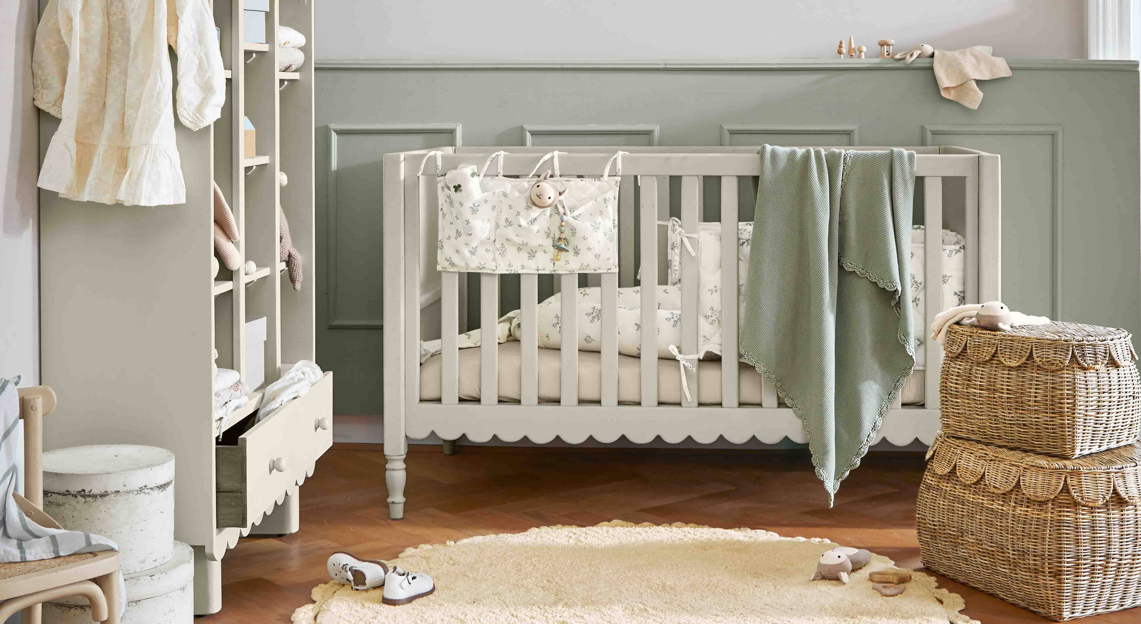 Cuna infantil de madera gris con manta verde y cestas de mimbre en habitación infantil acogedora