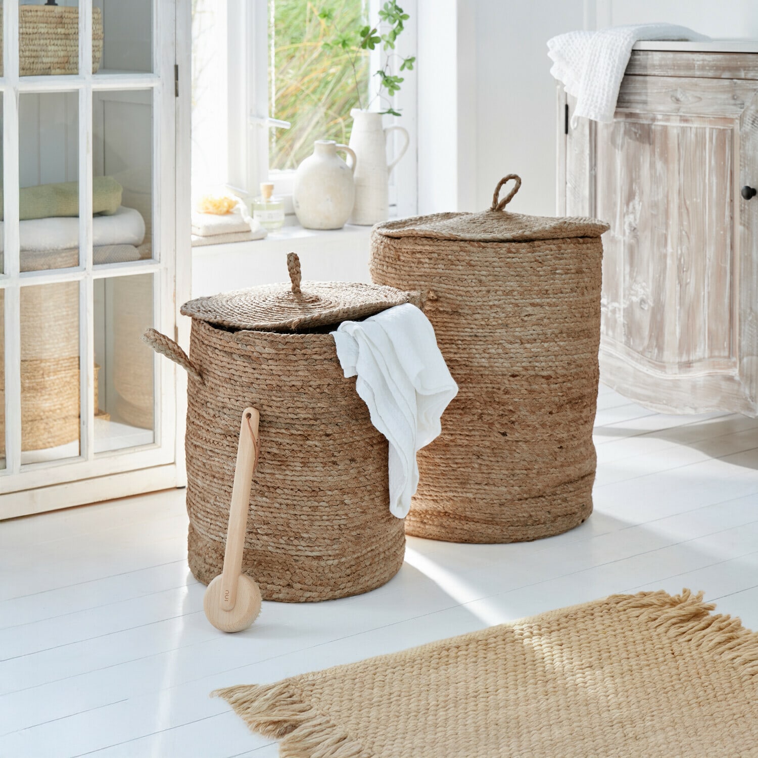 Set de 2 cestos para la ropa Kory Dos cestas redondas para ropa de yute natural beige en un baño luminoso