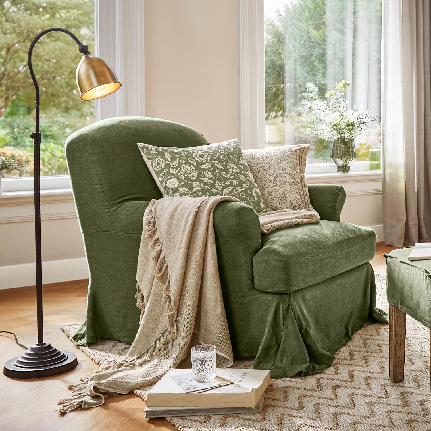 Sillón verde de tela con manta beige y cojines con estampado floral en sala luminosa