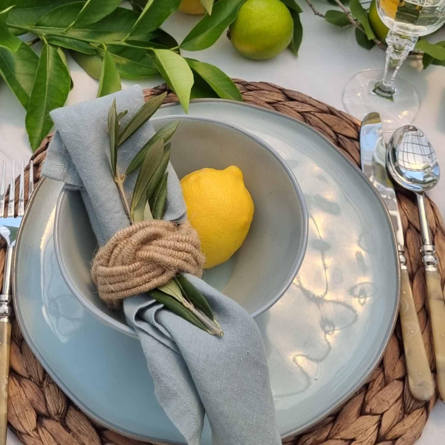 Vajilla de cerámica azul con servilleta de lino y limón sobre base de mimbre