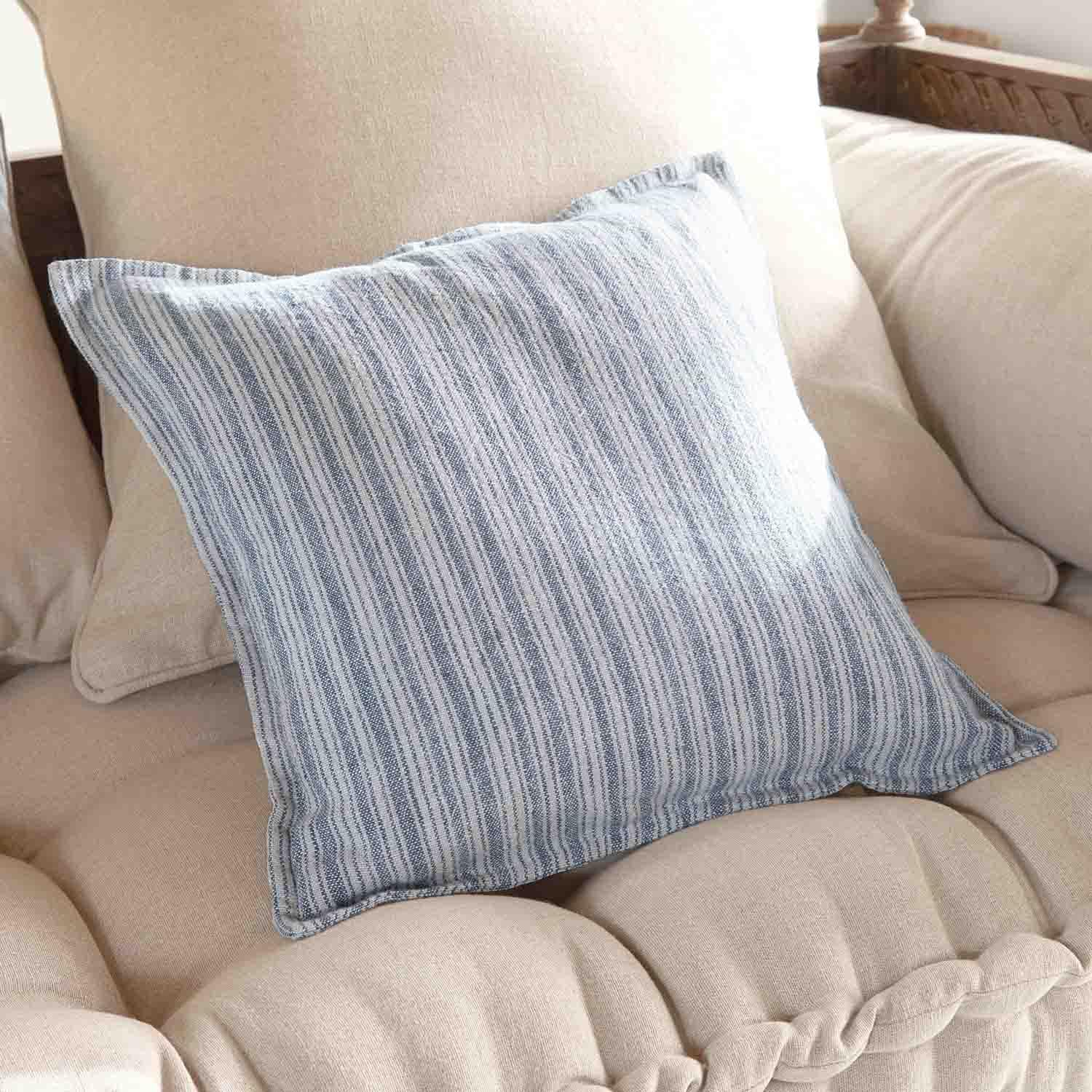 Cojín decorativo a rayas azules y blancas sobre sofá beige, tejido suave, estilo hogareño