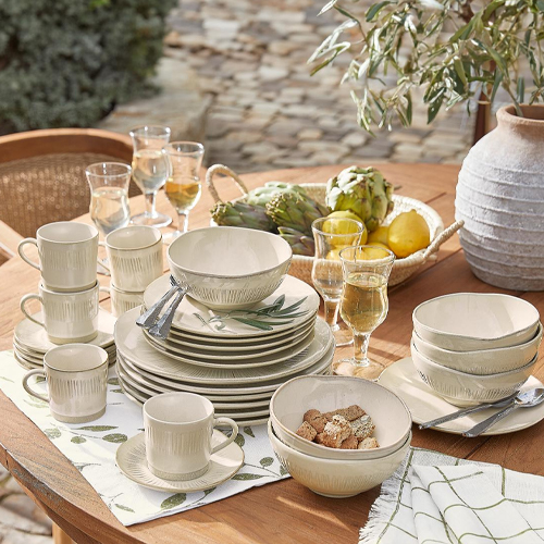 Juego de vajilla de cerámica crema con diseño de hojas verdes sobre mesa de madera al aire libre