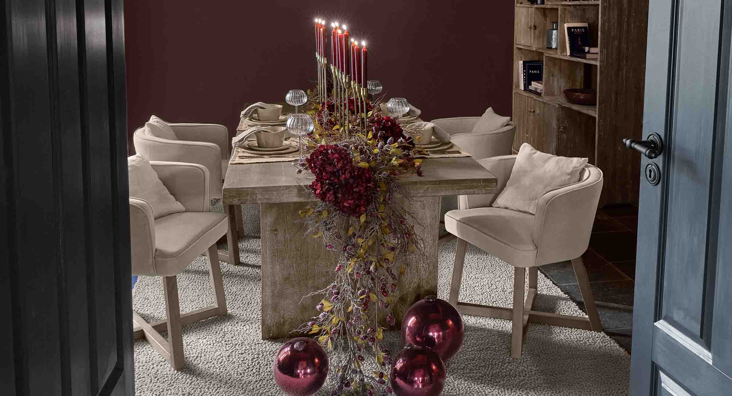 Mesa de comedor elegante con sillas beige y decoración festiva roja con velas encendidas