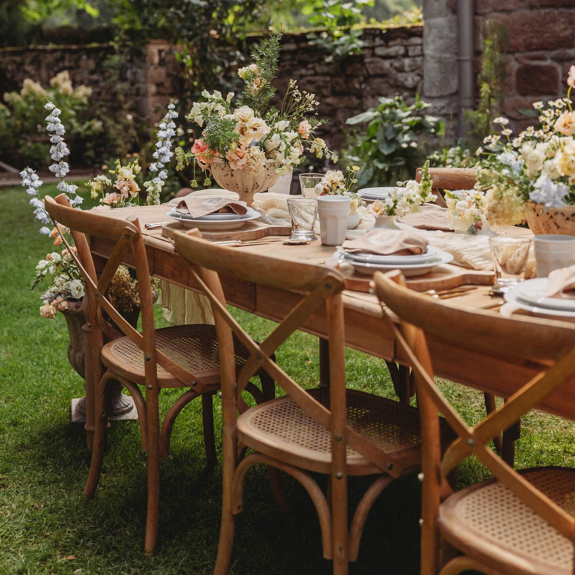 Mesa de jardín de madera con sillas de mimbre y decoración floral sobre césped verde